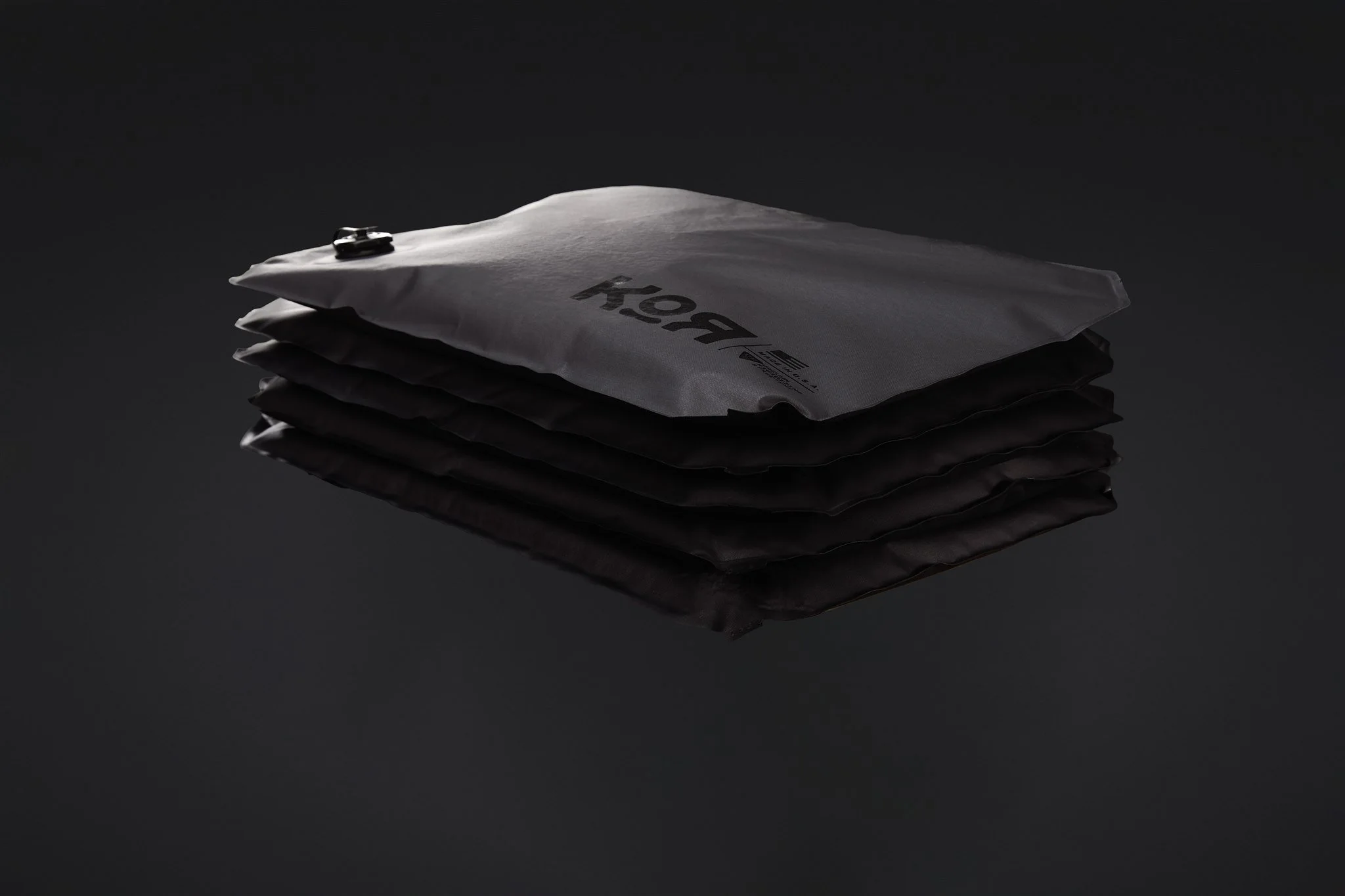 Stack of black and white envelopes or mailing bags, with one placed on top, on a reflective black surface.