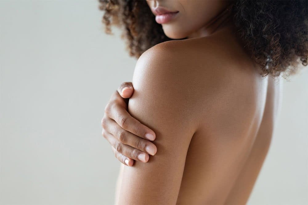 A woman with curly hair covering her chest with her hand, turned slightly to the side.