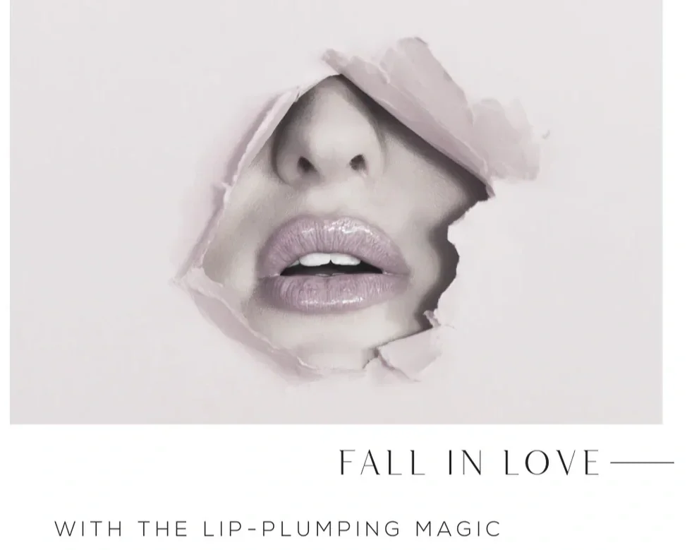 Close-up of lips and nose of a woman seen through a torn paper opening, with the text "Fall in Love — with the Lip-Plumping Magic" below.