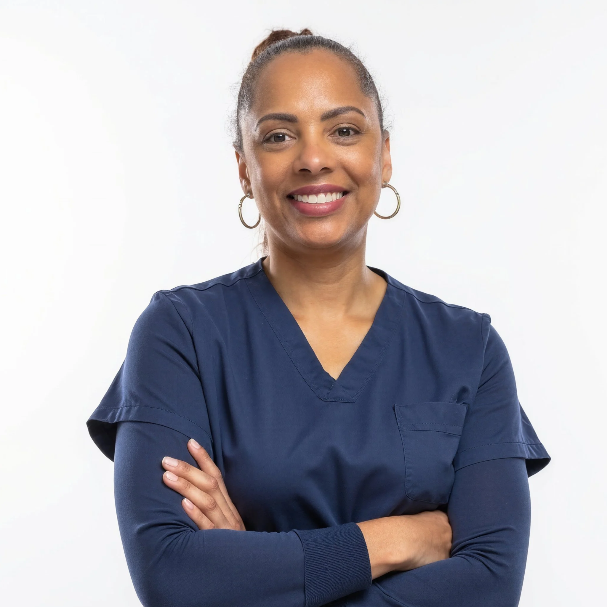 A smiling woman in navy medical scrubs standing with arms crossed against a plain white background.