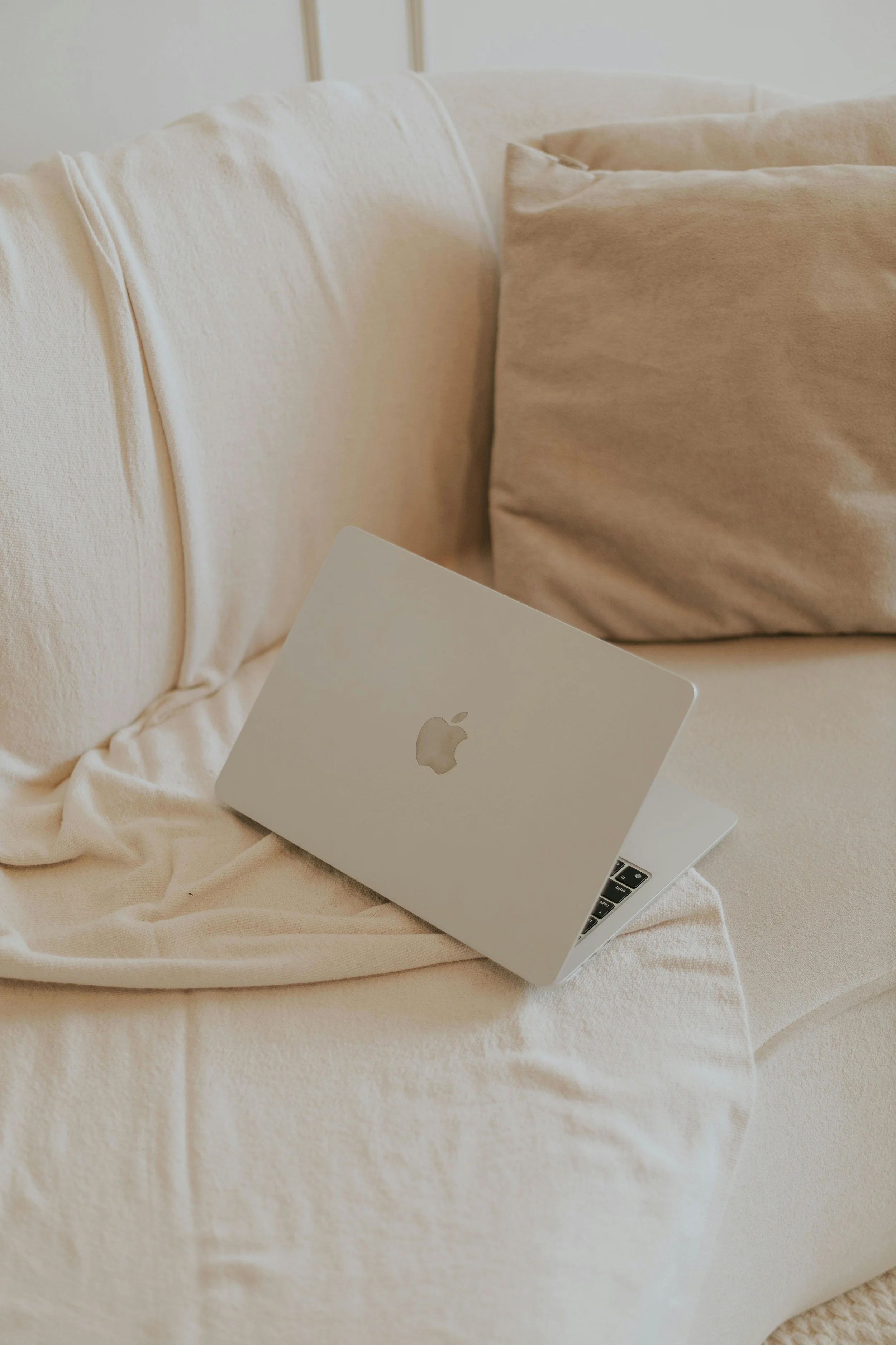 A silver MacBook laptop on a beige couch with beige cushions.