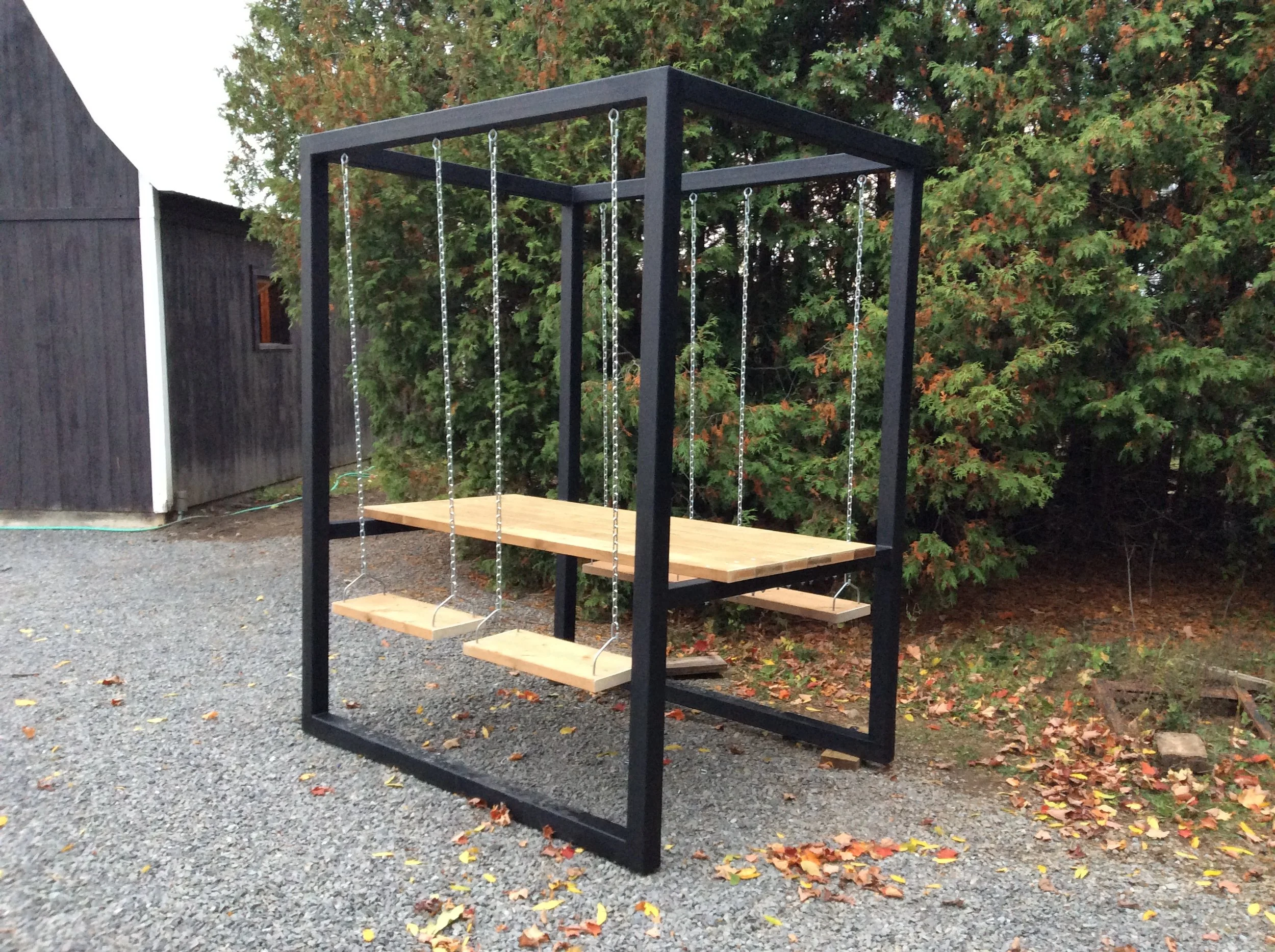 A black metal steel swing table in a backyard with trees and a gravel ground.