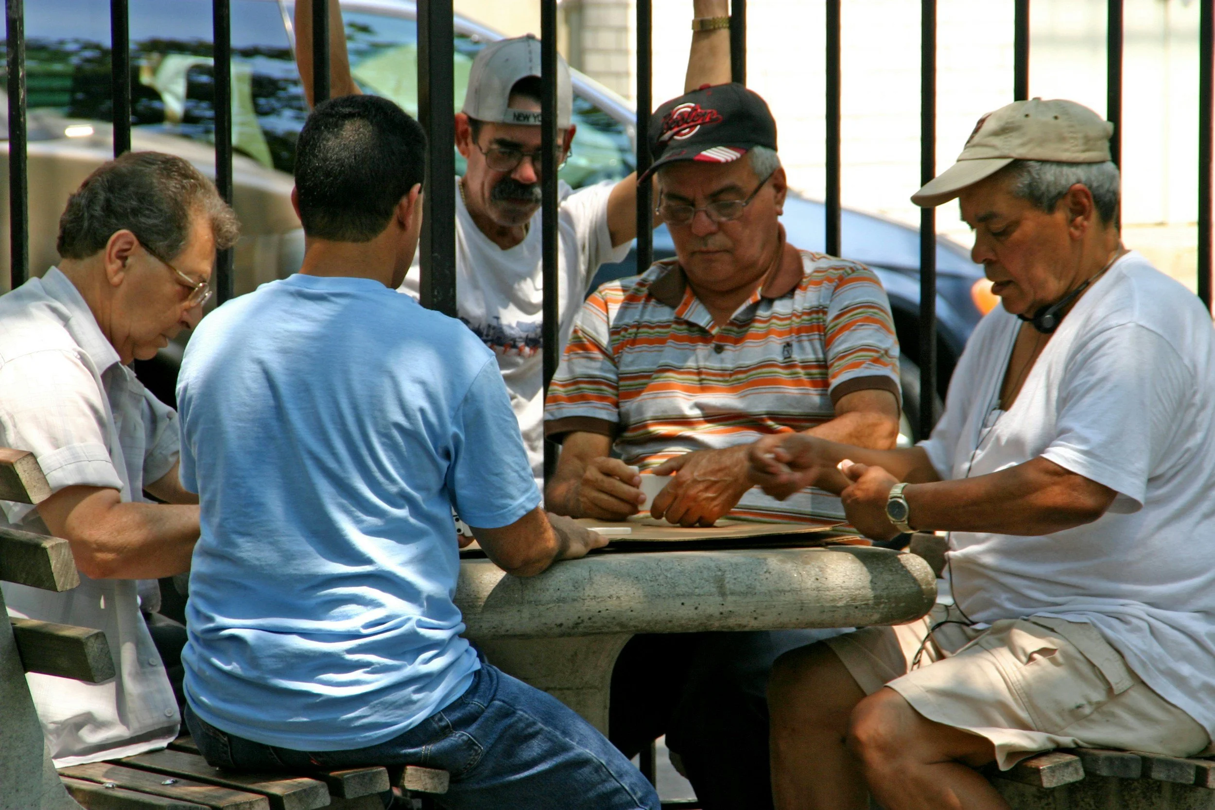 A group of four senior men gathered outdoors around a stone table, laughing and chatting.