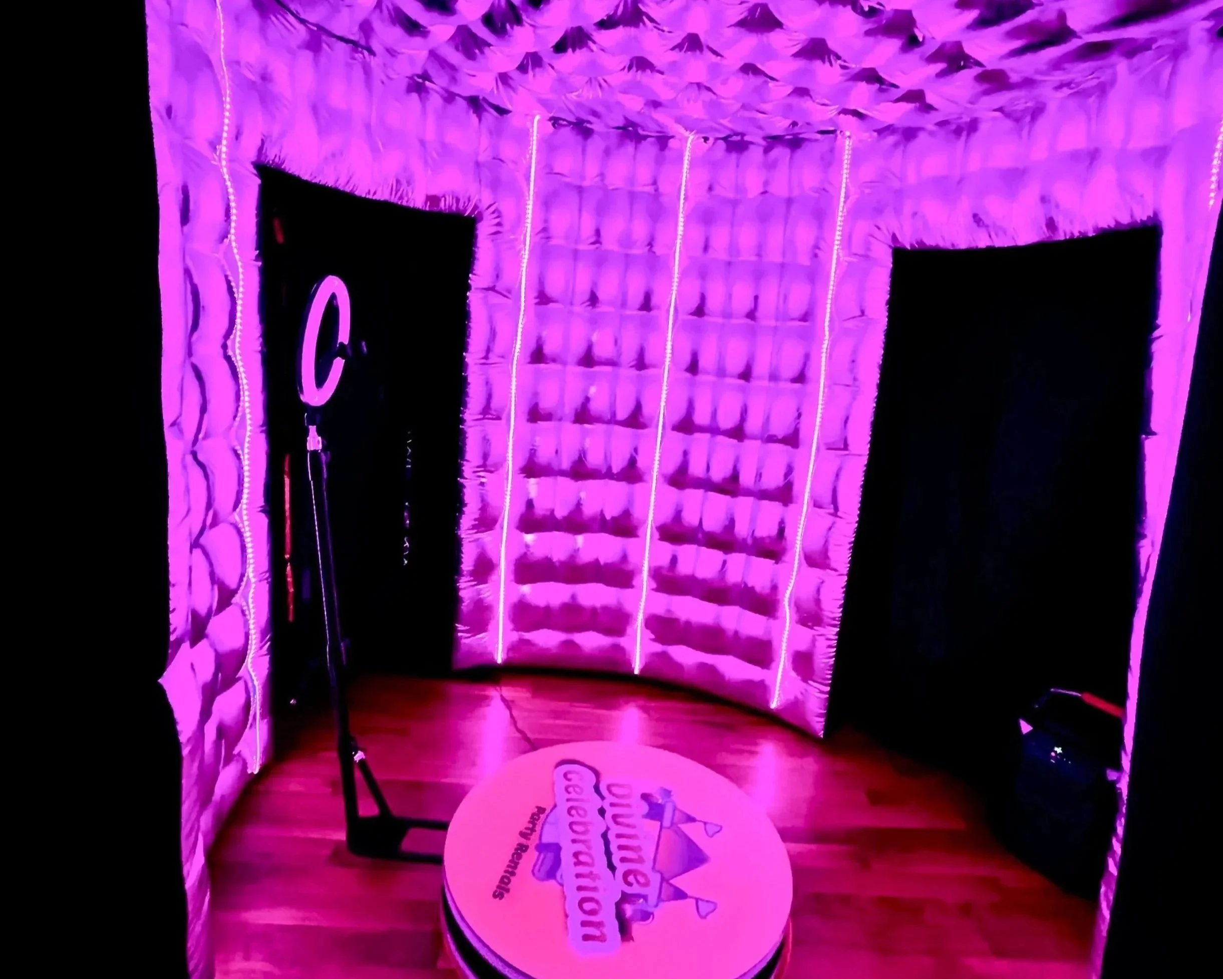 A soundproof booth with purple lighting, padded walls, a microphone stand, and a round sign on the floor that reads 'Ultimate Celebration' with a crown graphic.
