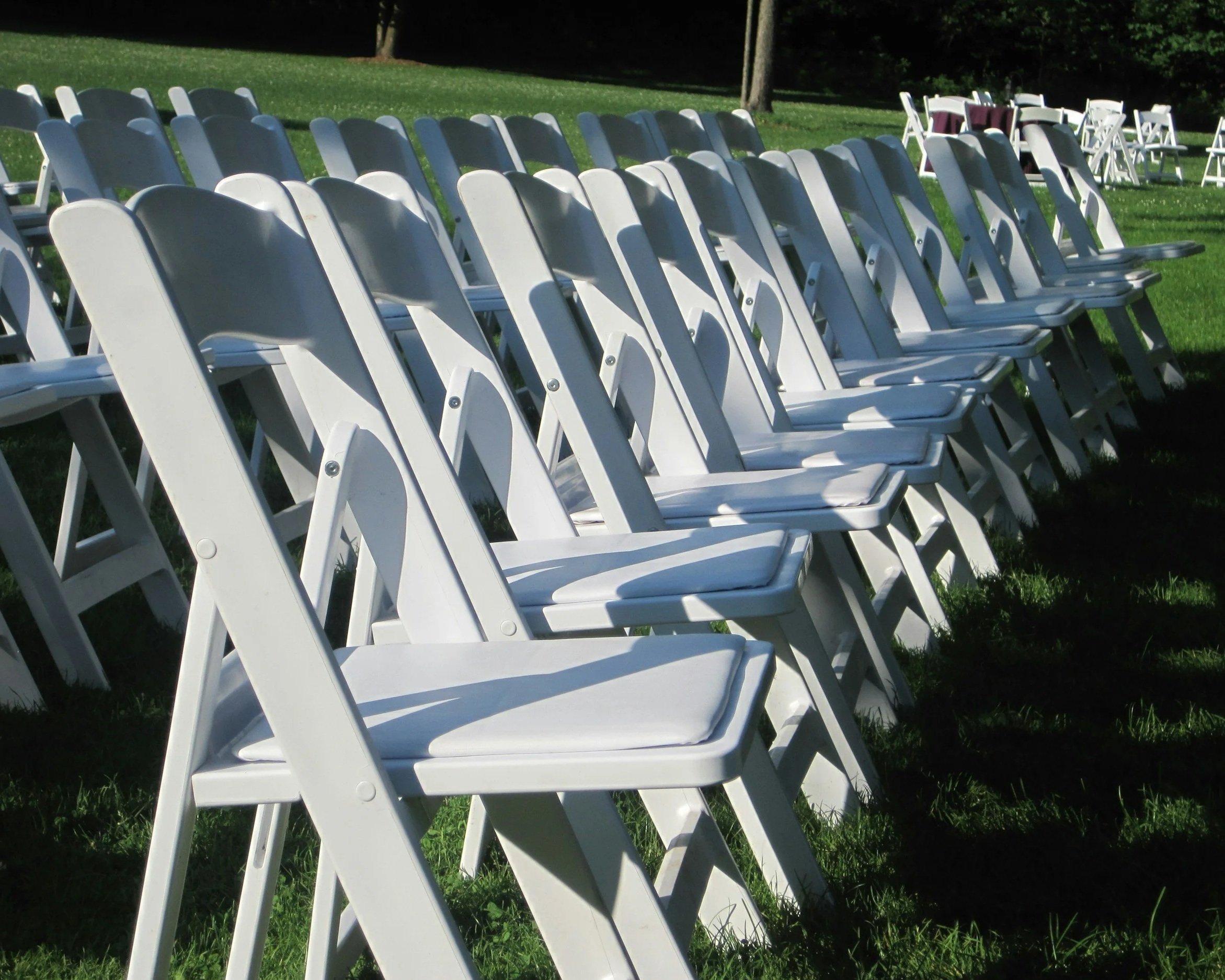 Multiple white folding chairs arranged on green grass, likely set up for an outdoor event or ceremony.
