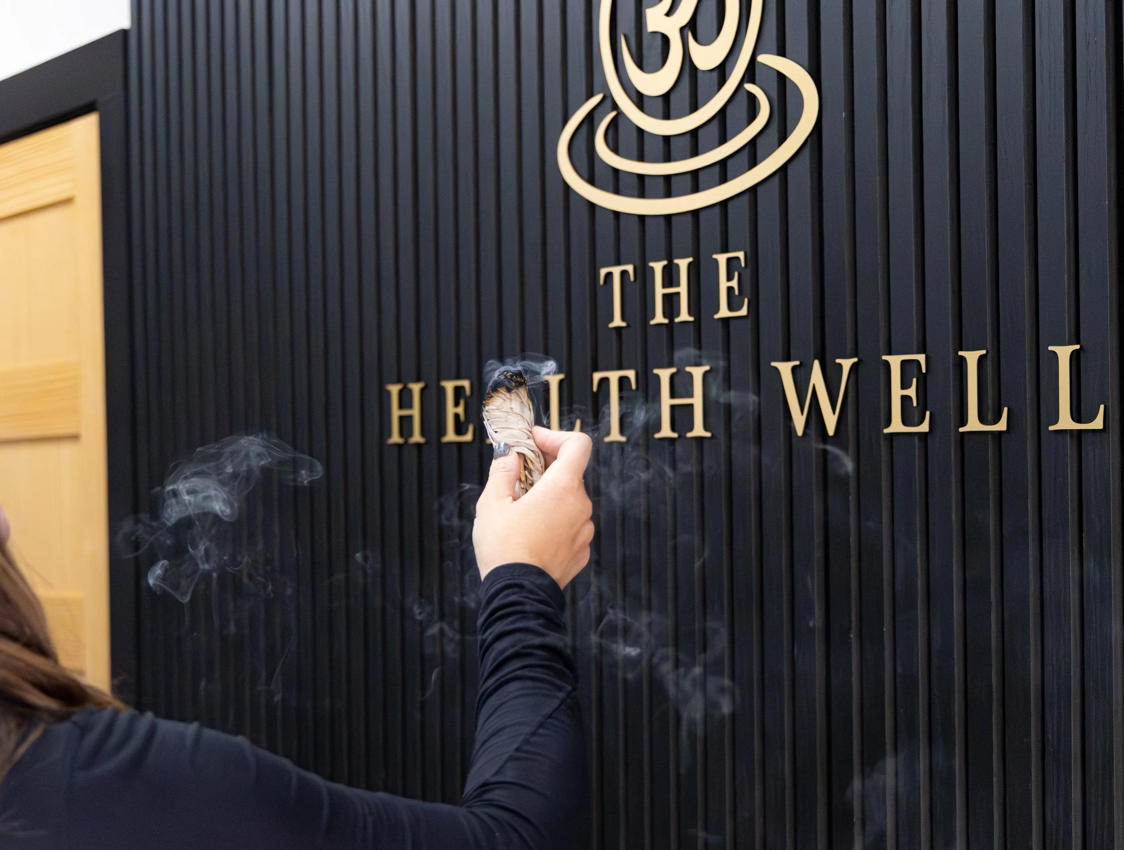 Person wiping or cleaning a black wall with gold lettering that reads 'The Health Well' and a large decorative icon above the text.