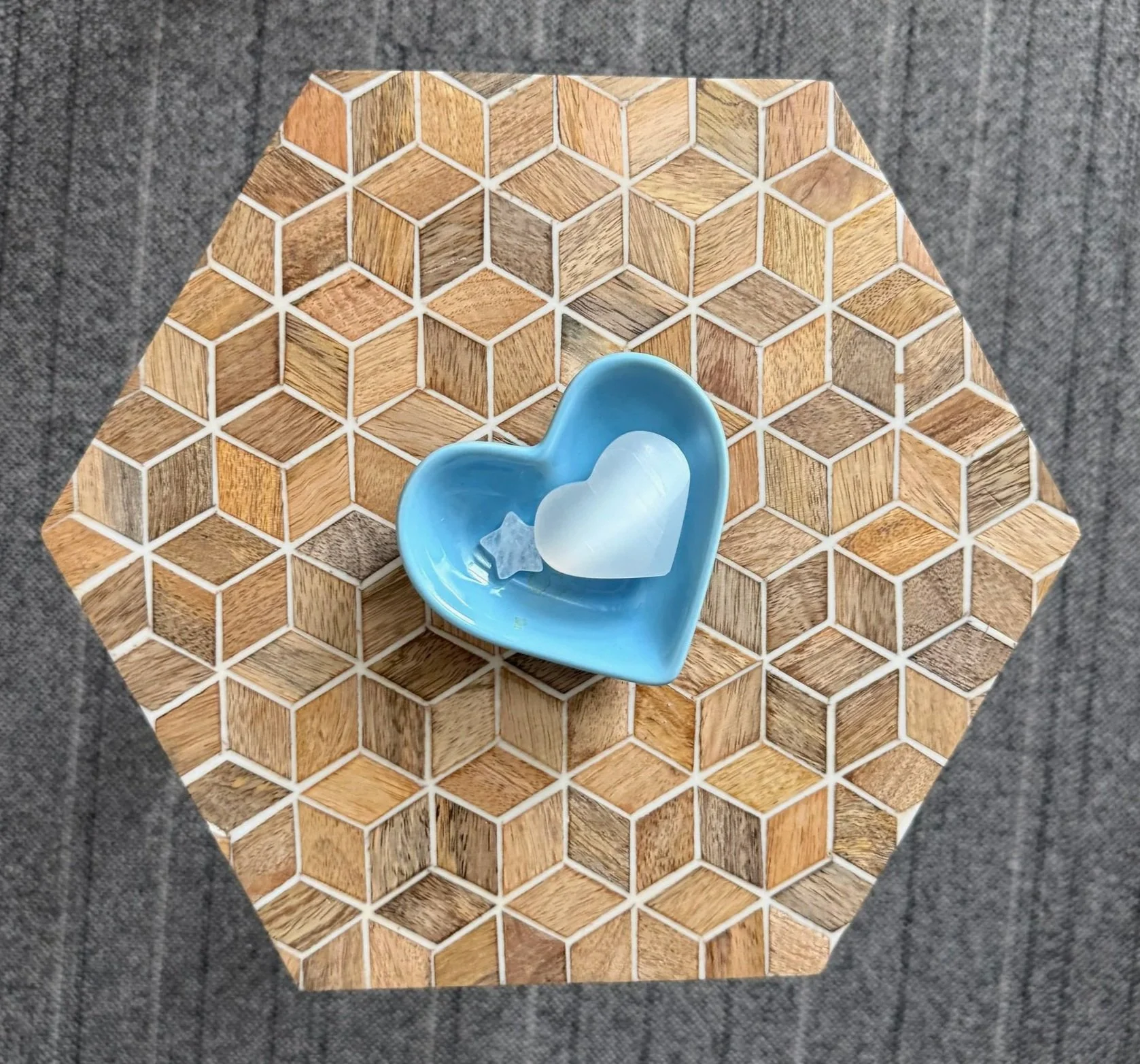 A blue heart-shaped dish with a white heart and star-shaped objects, placed on a wooden hexagonal tile surface.