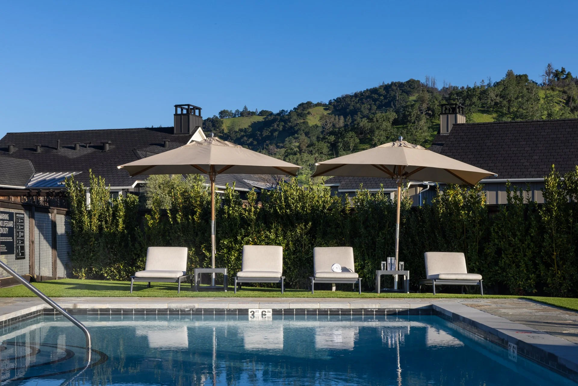 Swimming pool with lounge chairs, umbrellas, and a scenic hillside in the background.