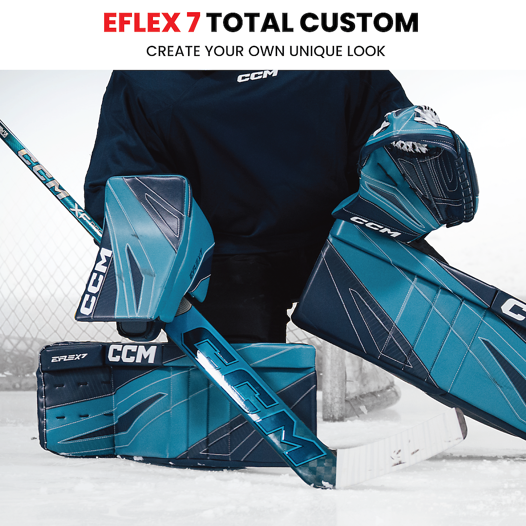 Hockey goalie in black jersey and blue CCM goalie gear, including pads, blocker, and stick, on ice rink.