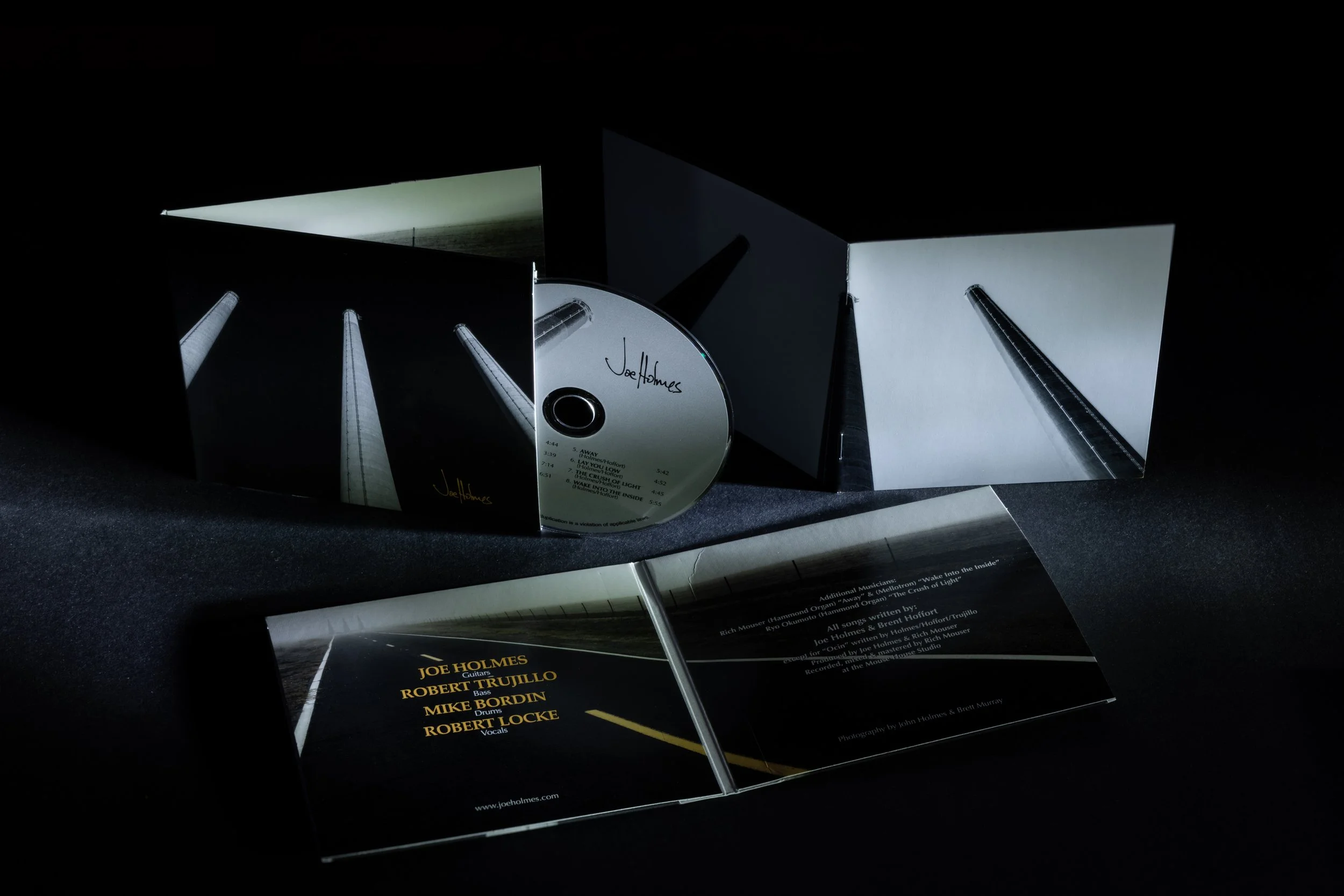 Open CD case with booklet and disc, featuring band member Joe Holmes and song list, set against a black background.