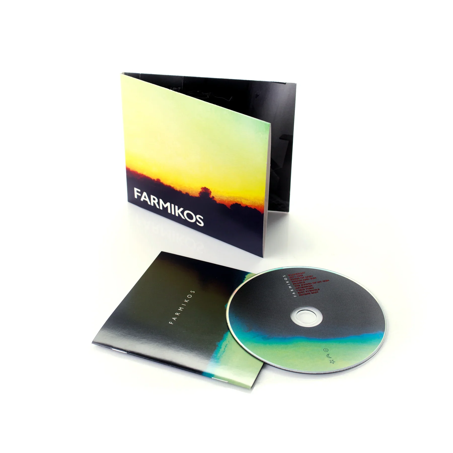 A booklet titled "FARMIKOS" featuring a sunset over a silhouette of trees on the cover, a CD with a holographic surface, and an open booklet displaying red text.