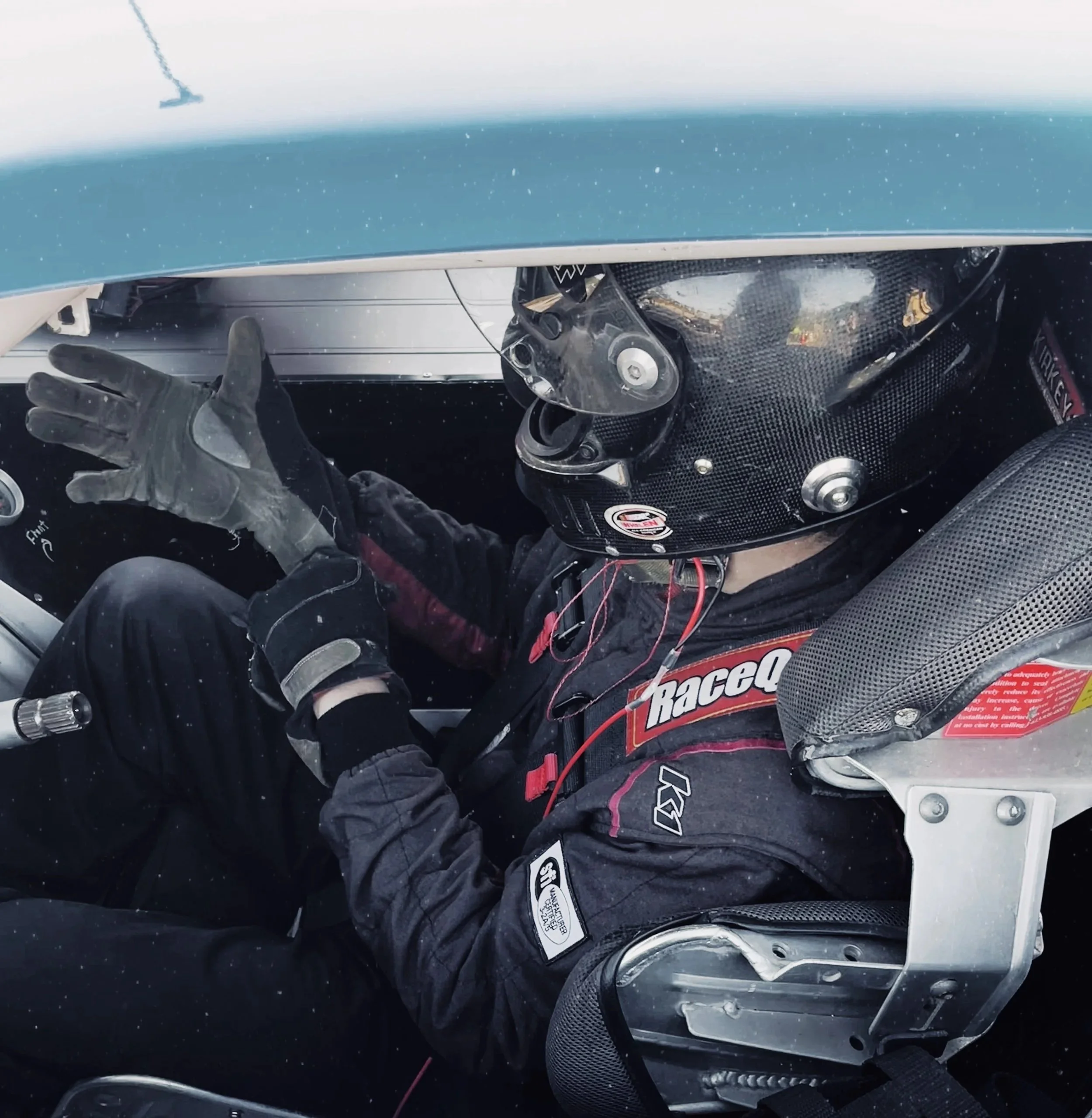 Close-up view of a race car driver putting gloves on in cockpit of race car. 