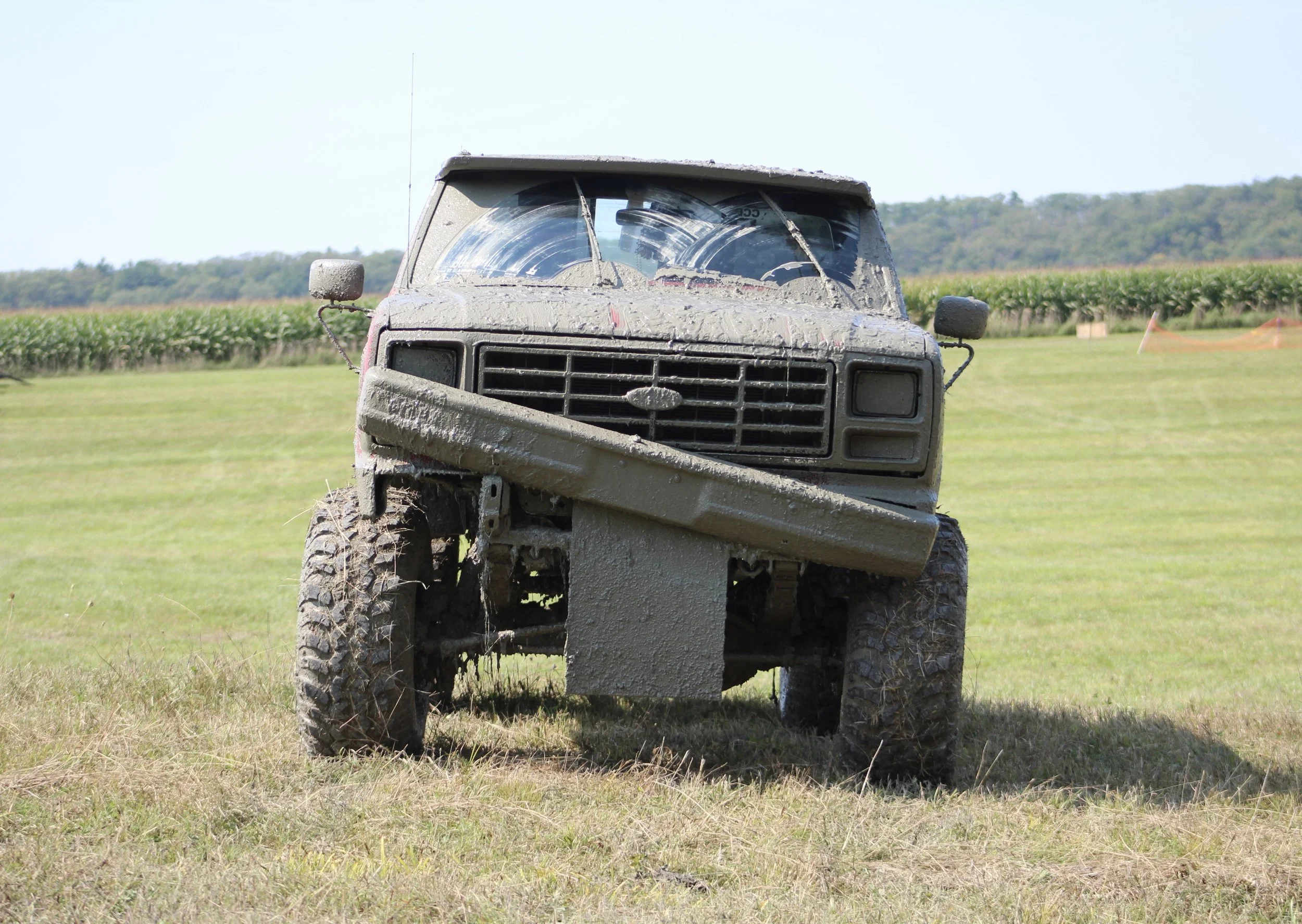 A muddy, overturned pickup truck in a grassy field with a backdrop of trees and hills.