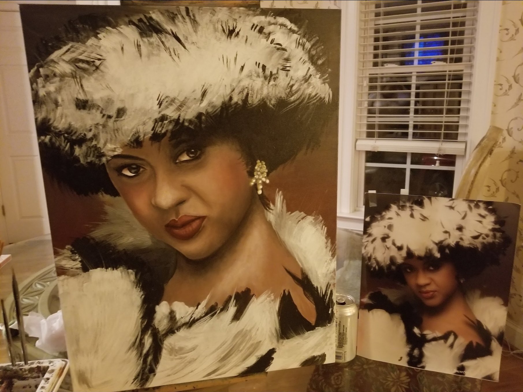 Painting and print of a woman wearing a large feathered hat and earrings, with dark makeup and a neutral expression, displayed on a table next to a soda can in a room with a window and floral wallpaper.