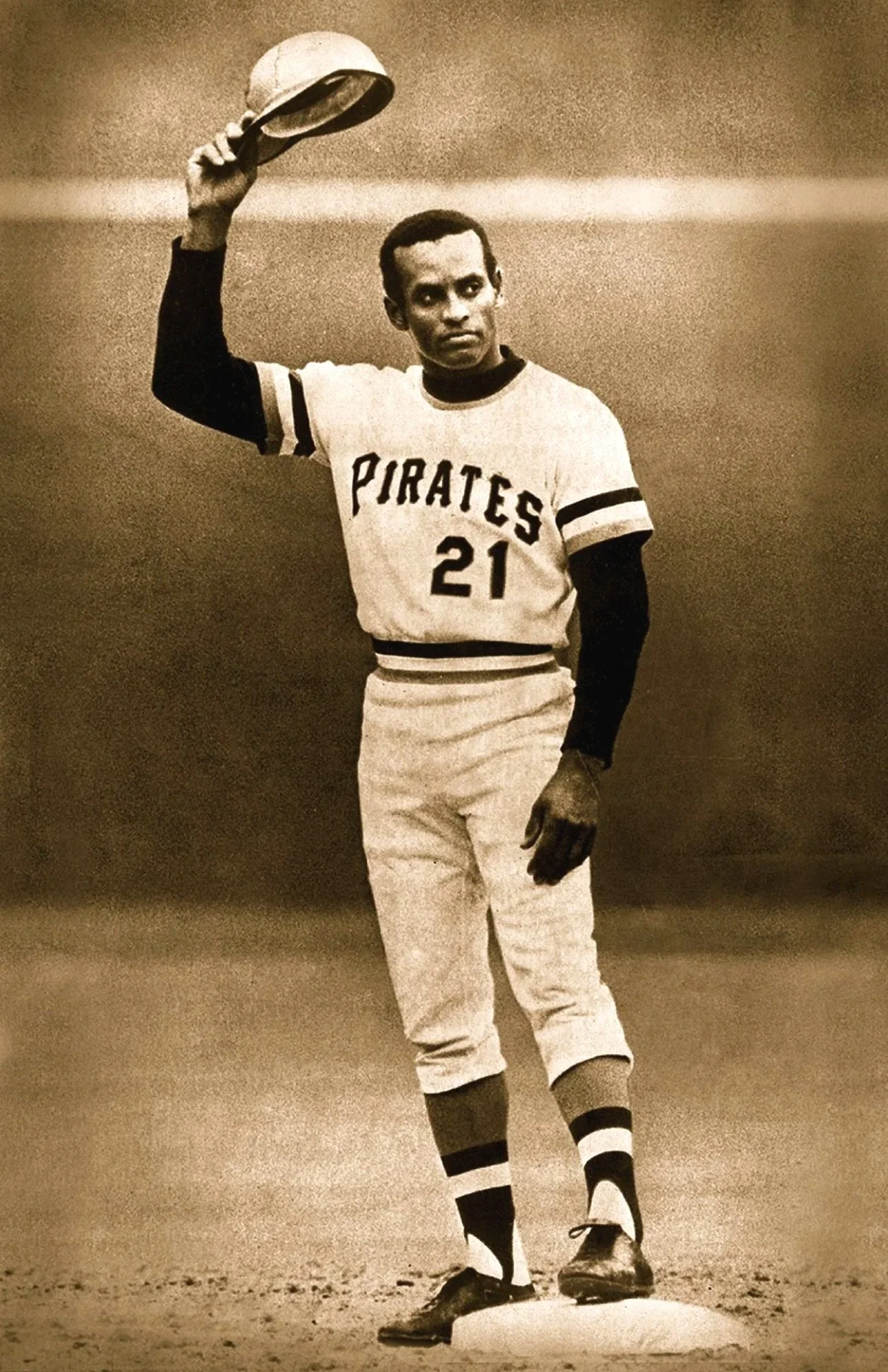A black-and-white photo of a baseball player wearing a Pittsburgh Pirates uniform, holding a hat in the air.