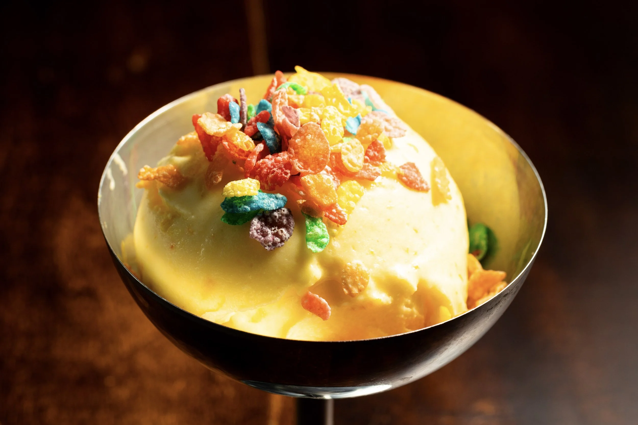 Scoops of vanilla ice cream topped with colorful cereal pieces in a metal serving dish.