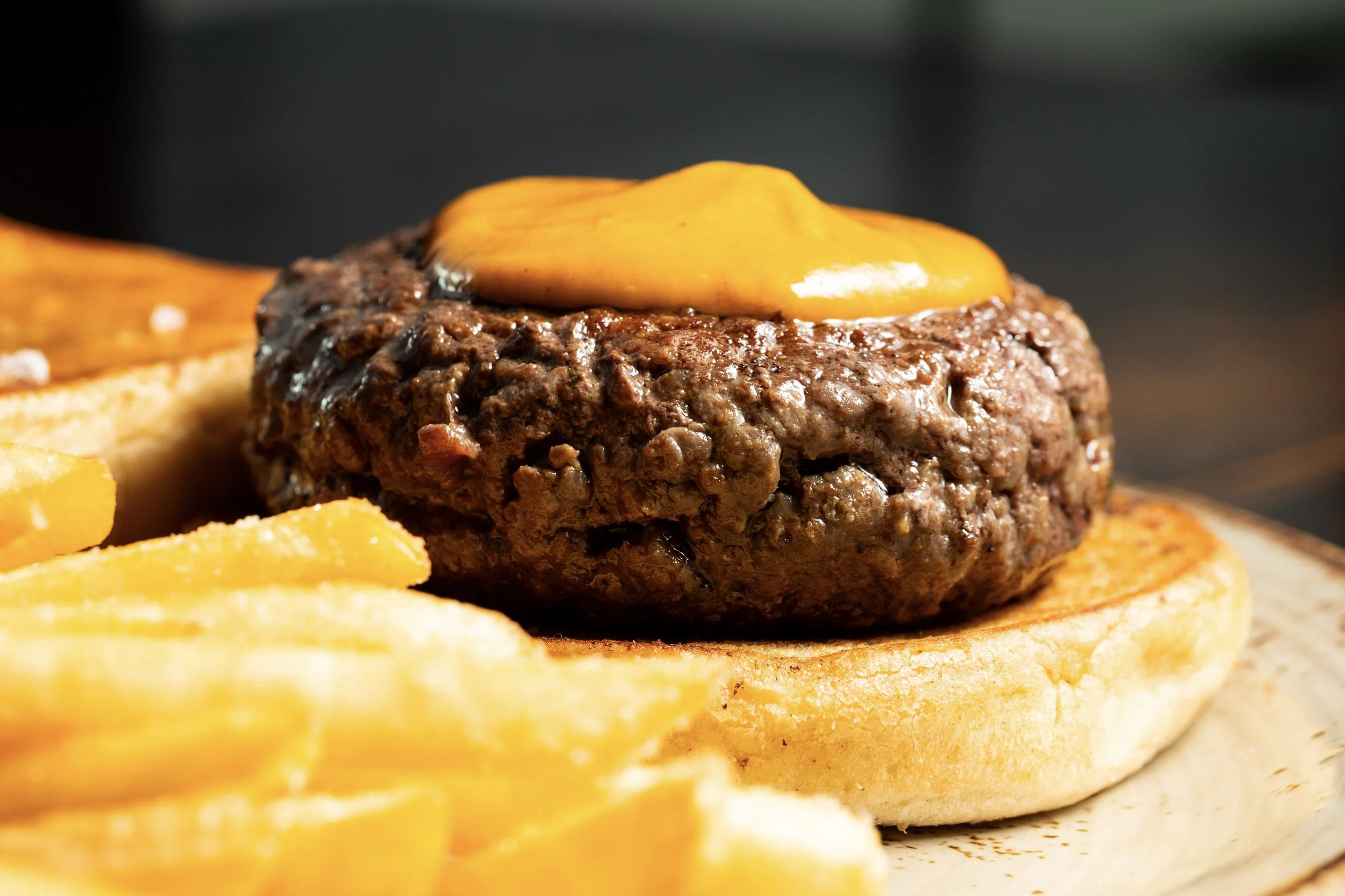 Close-up of a beef patty with melted cheese on grilled bun, with side of French fries