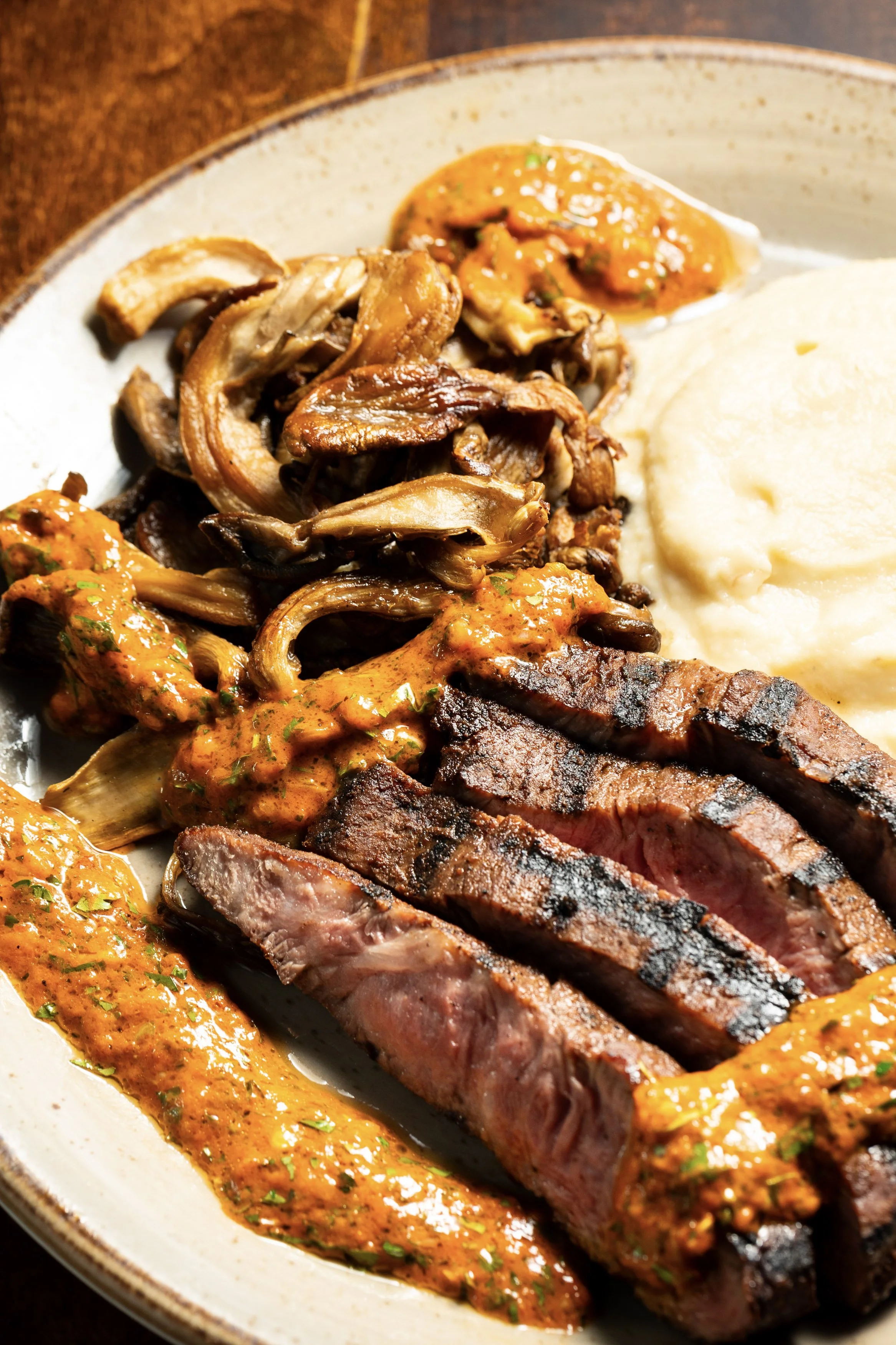 Steak with grilled grill marks, sautéed mushrooms, mashed potatoes, and spicy sauce on a plate.