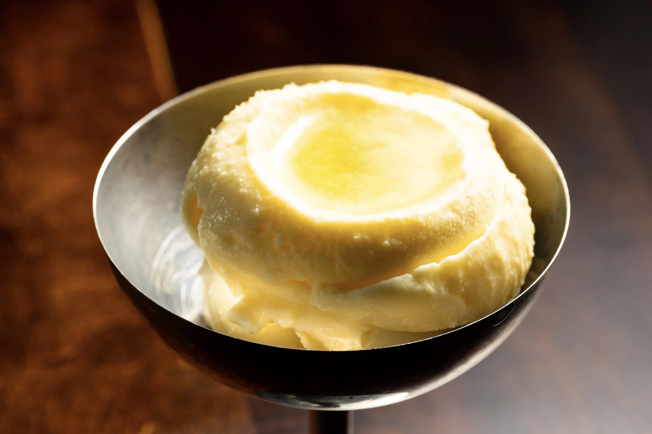 A metal bowl filled with lemon-flavored ice cream garnished with a lemon slice.