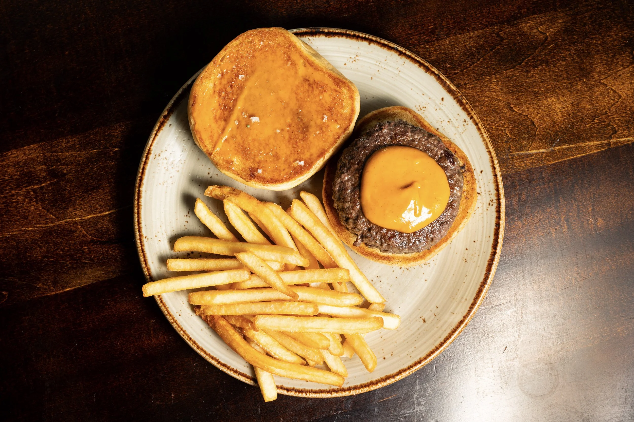 Hamburger with a fried egg on top, served with French fries on a round ceramic plate on a wooden table.