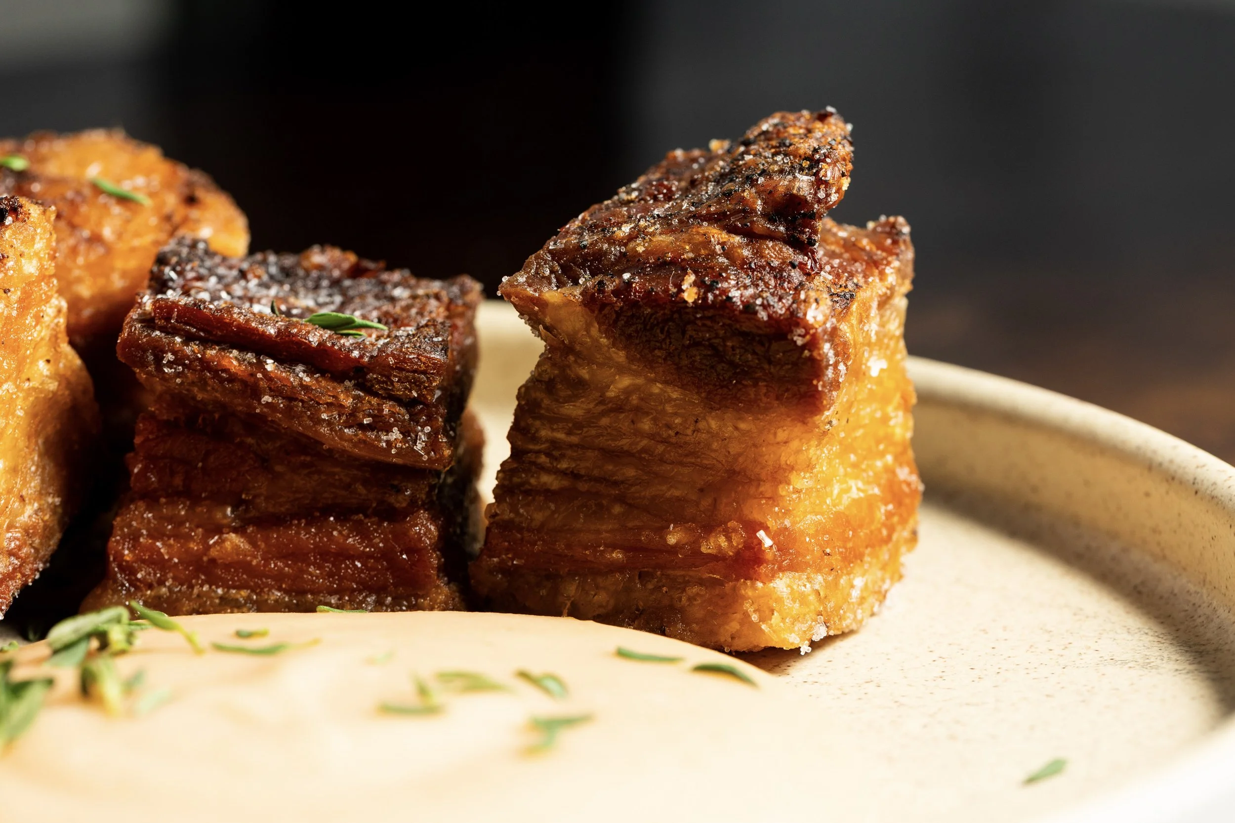 Close-up of crispy, grilled pork belly pieces on a beige plate.