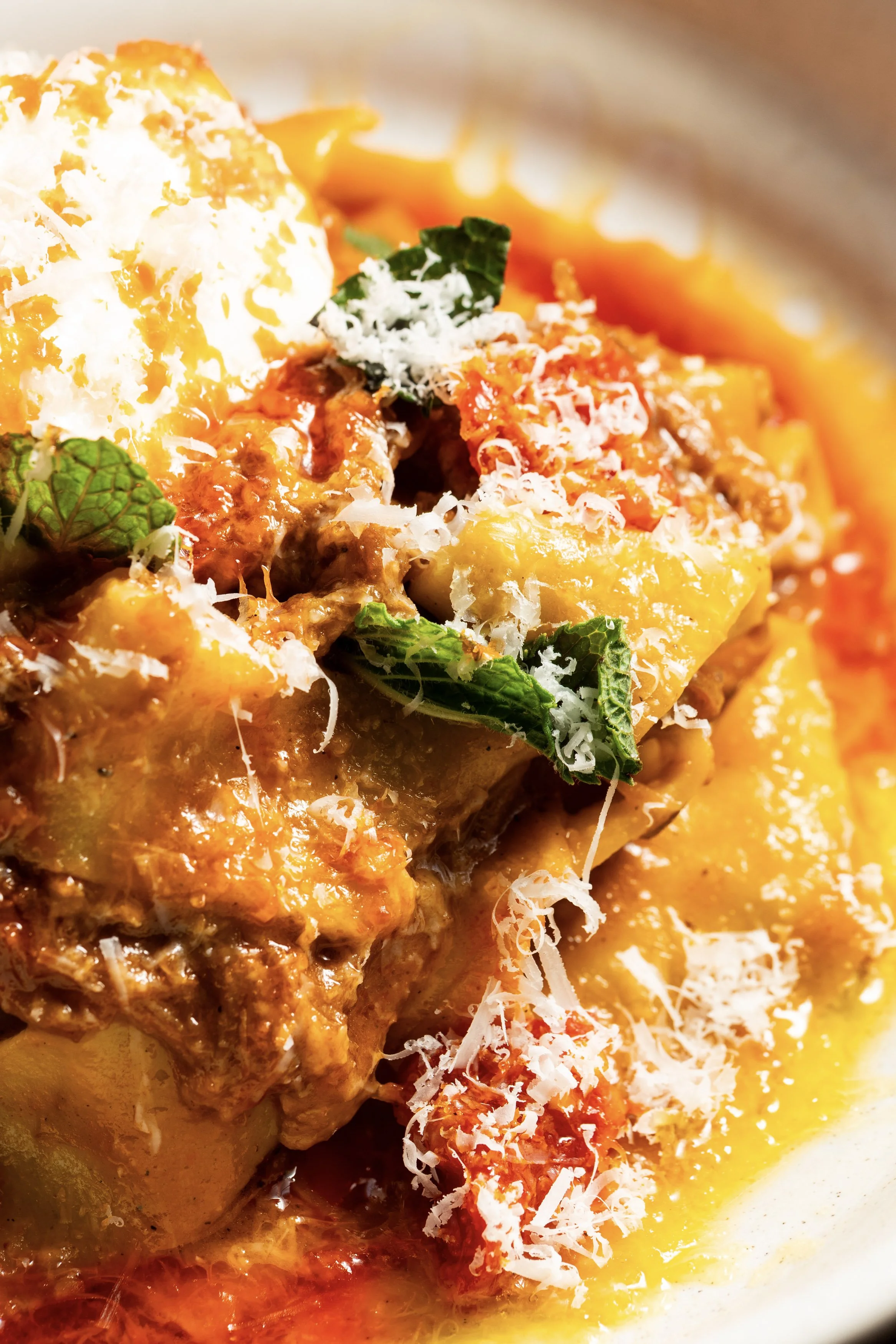 Close-up of a baked casserole dish with shredded cheese, green herbs, and tomato sauce, topped with shredded cheese and sauce.