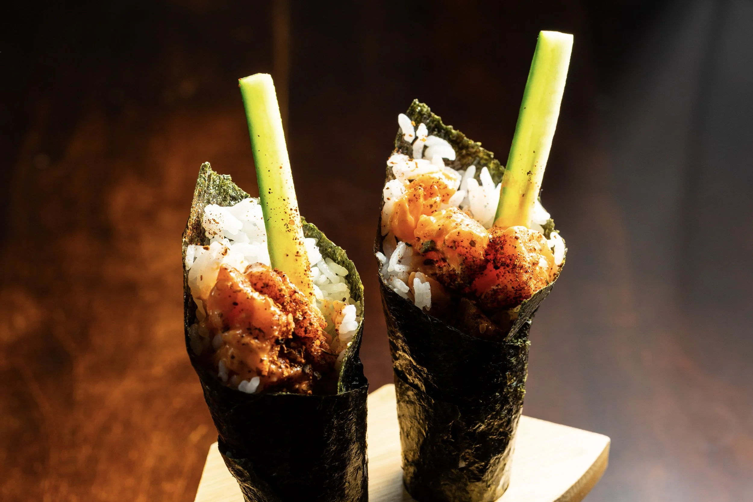 Two sushi hand rolls with seaweed wrapping, rice, deep-fried seafood filling, and green scallions.