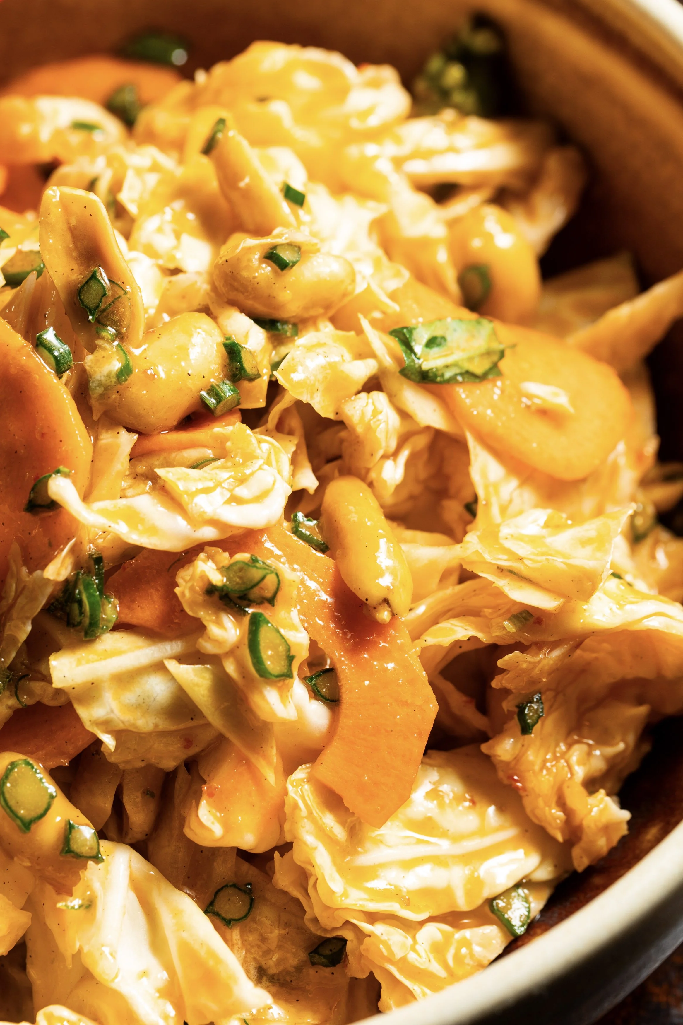 Close-up of a salad with shredded cabbage, sliced carrots, chopped green onions, and diced egg, all coated in a creamy dressing.