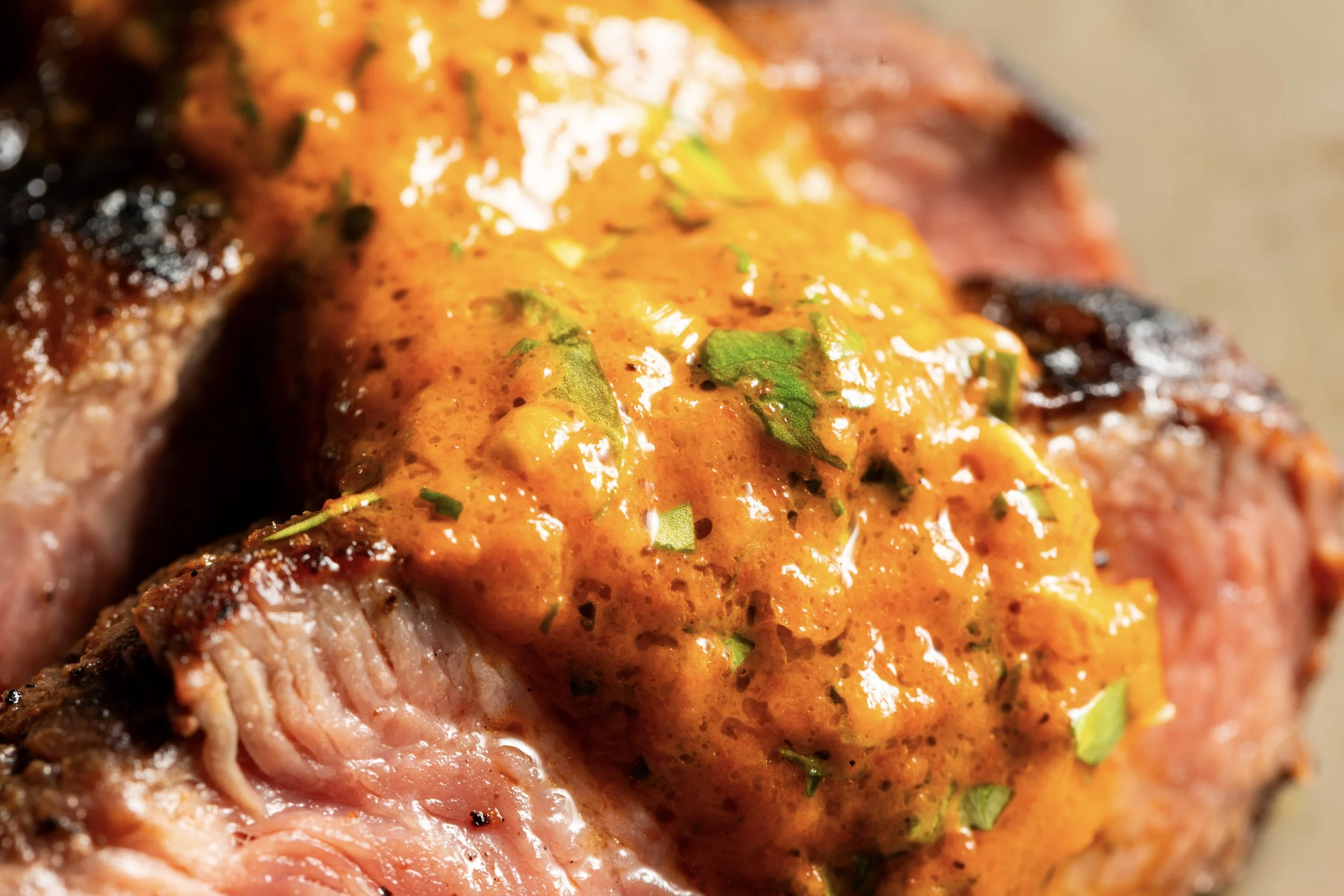 A close-up of a cooked steak topped with orange sauce and garnished with green herbs