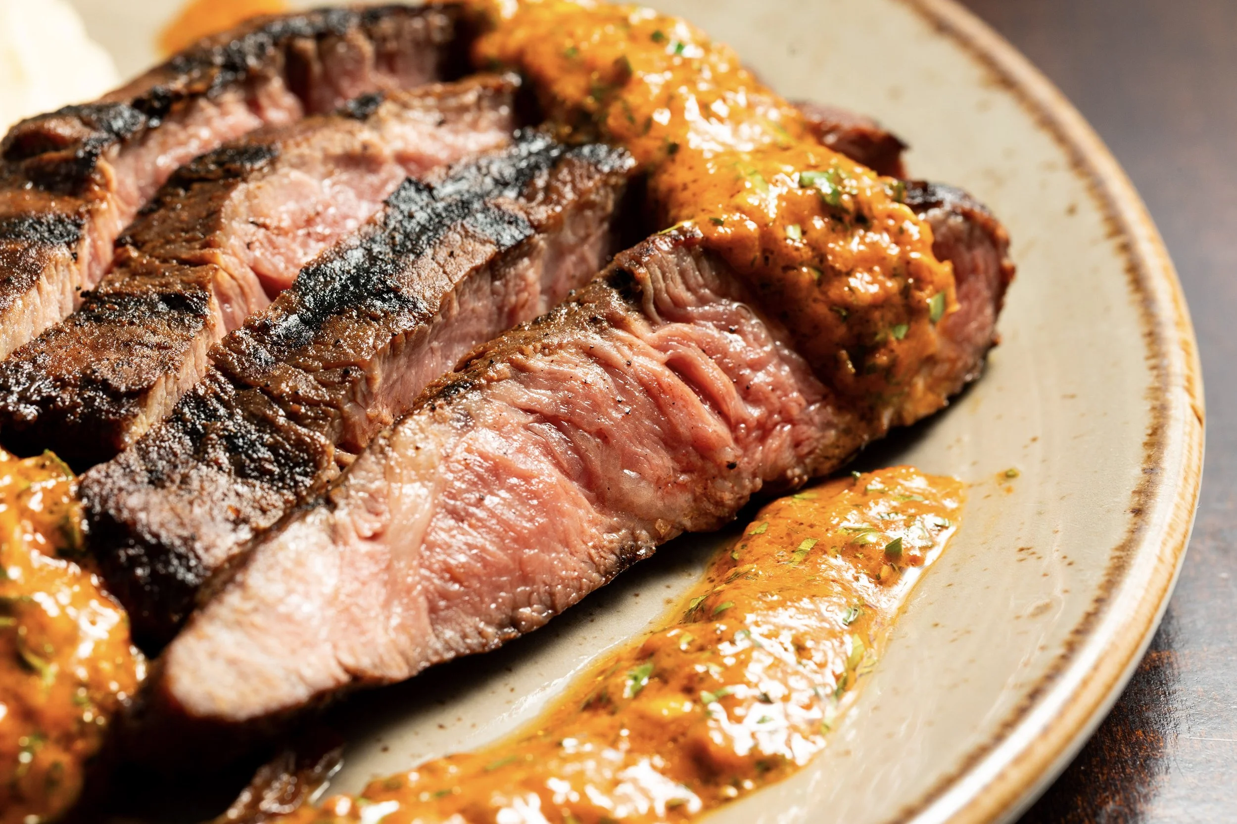 Close-up of sliced, grilled steak with a side of orange sauce or chutney on a beige plate.
