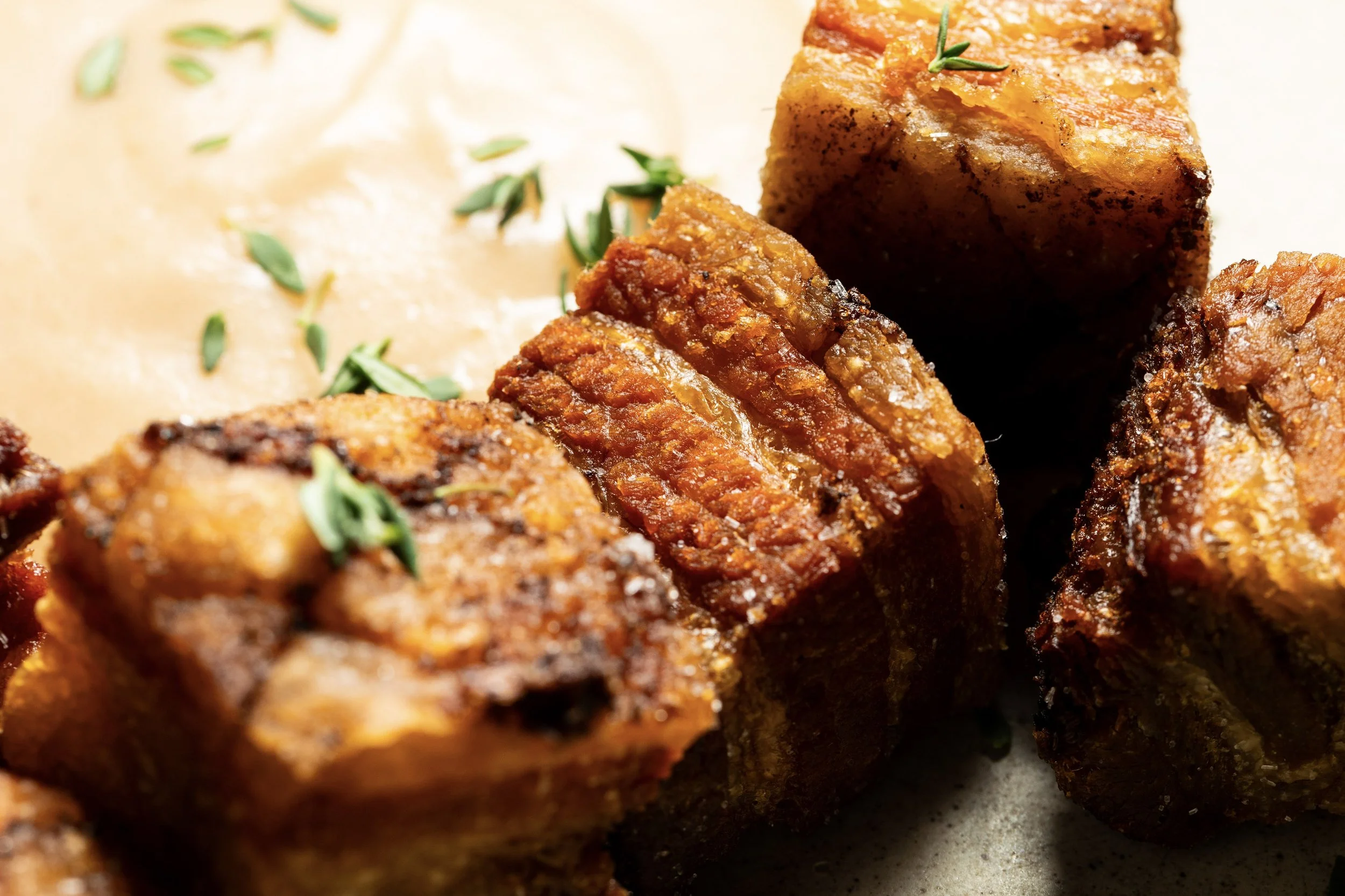 Close-up of crispy, cooked meatloaf slices garnished with fresh herbs, with a creamy sauce and chopped herbs in the background.