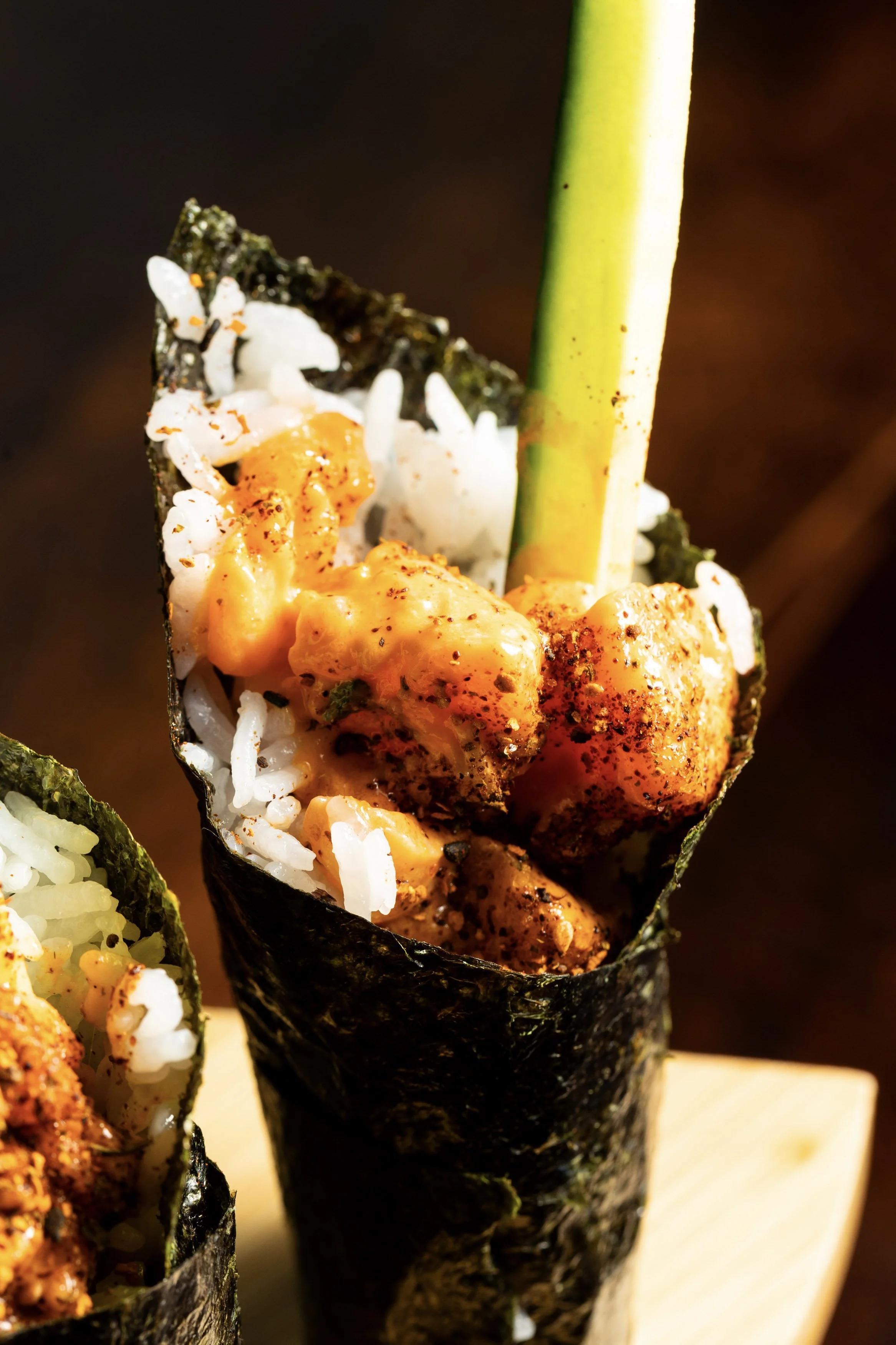 Close-up of a sushi hand roll with rice, seaweed, spicy salmon, and a cucumber stick.