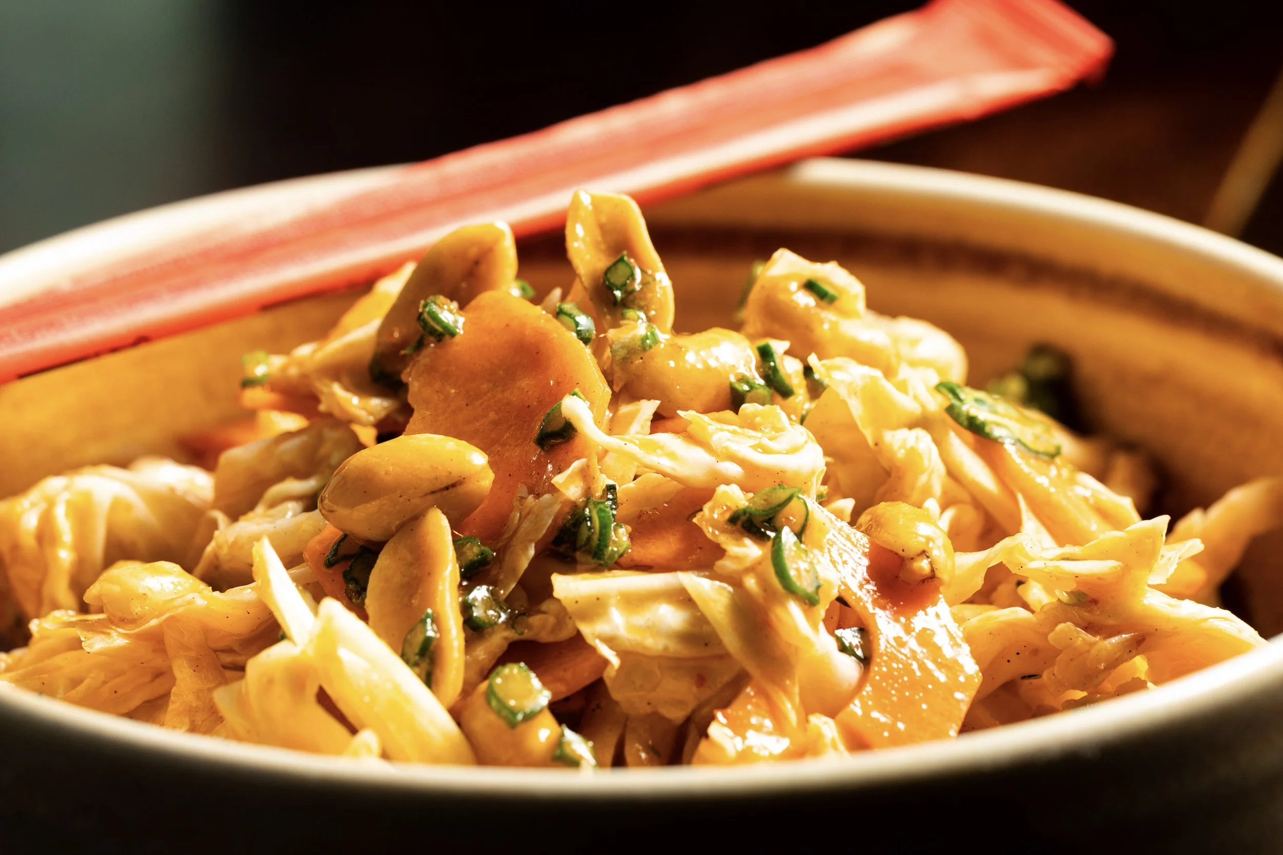 Close-up of a bowl filled with shredded cabbage, sliced mushrooms, chopped green onions, and sliced carrots.
