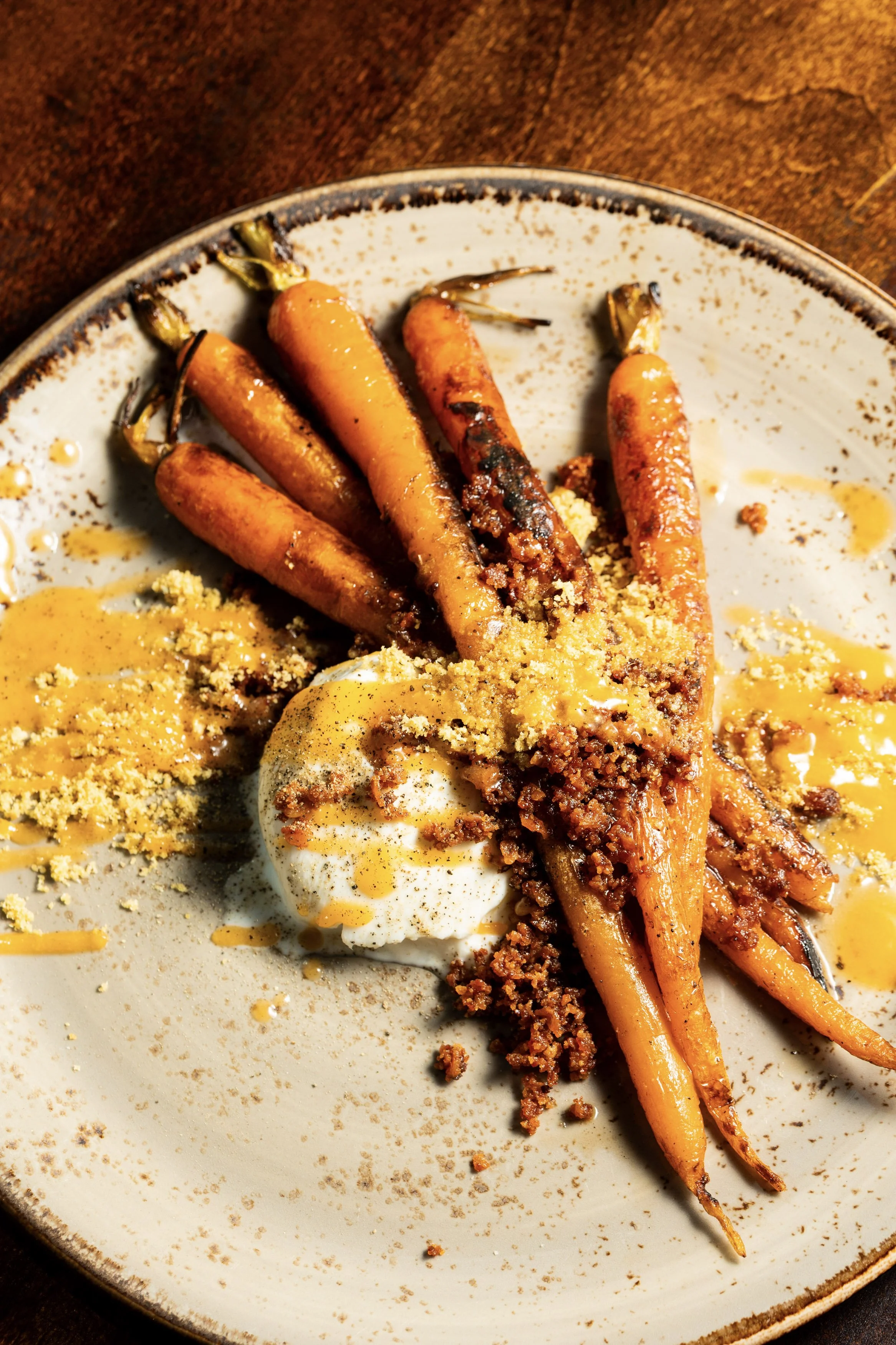 Roasted baby carrots topped with crumbled bacon, chopped nuts, and a dollop of cream or sauce on a ceramic plate.