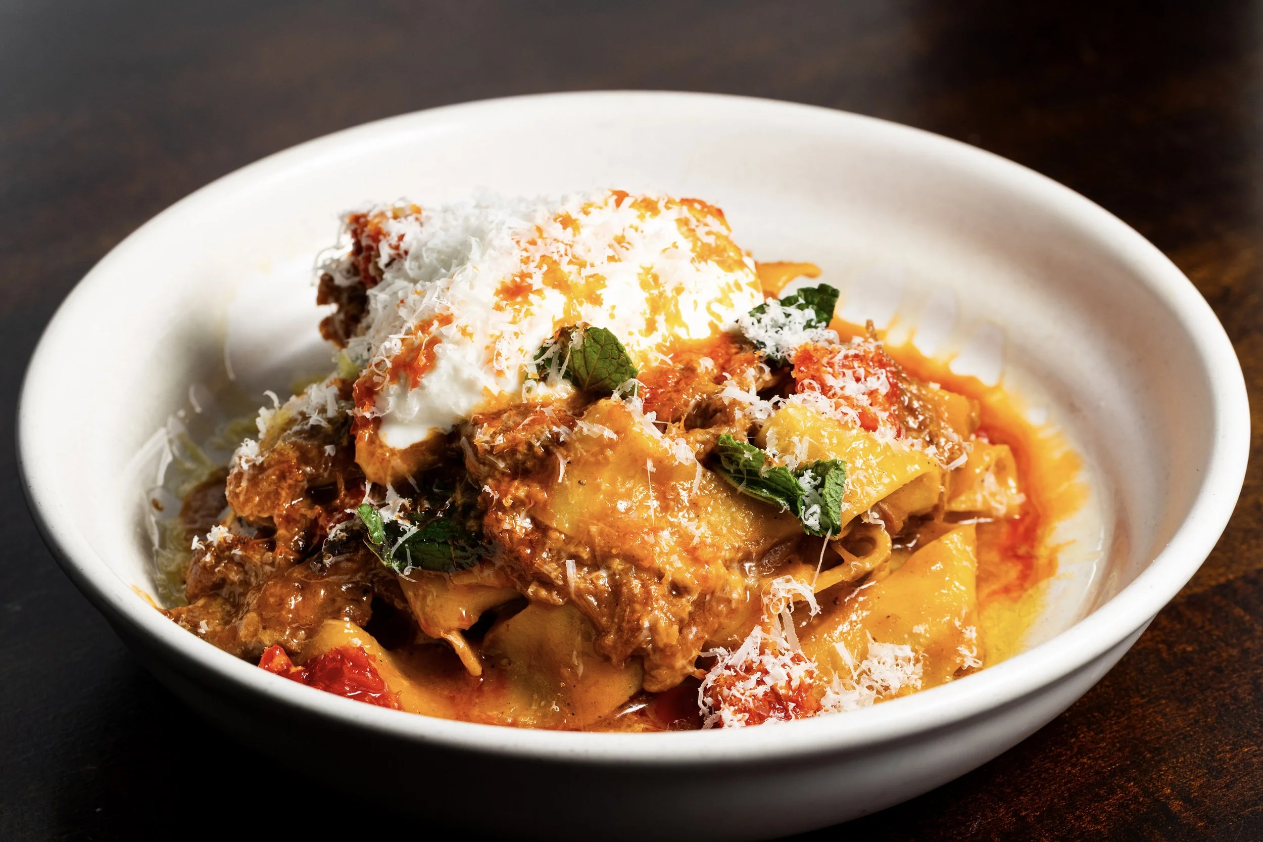 Bowl of beef and vegetable stew topped with shredded cheese, sour cream, and fresh herbs