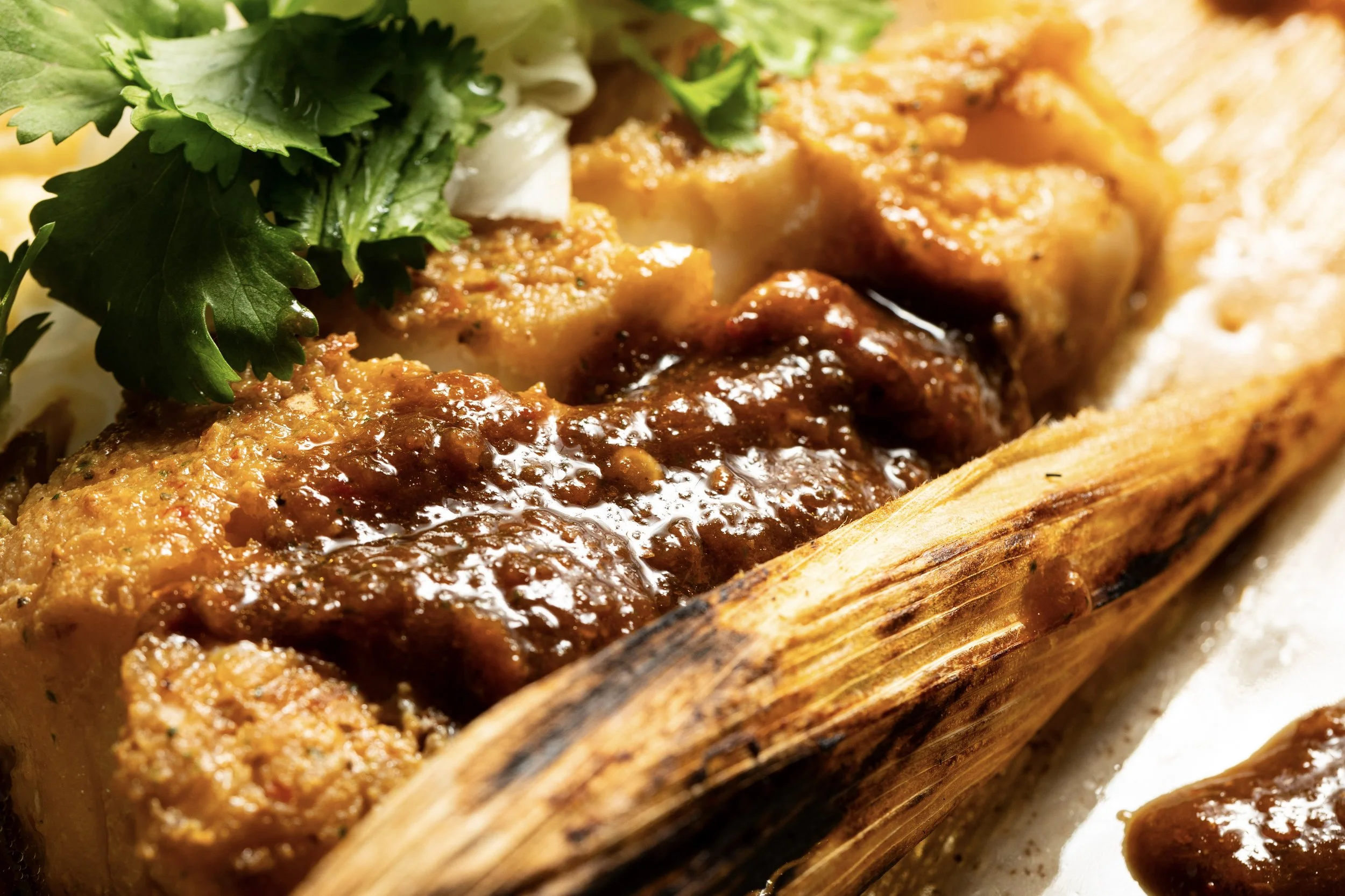 Close-up of a roasted plantain topped with savory meat sauce, garnished with cilantro and chopped onions.