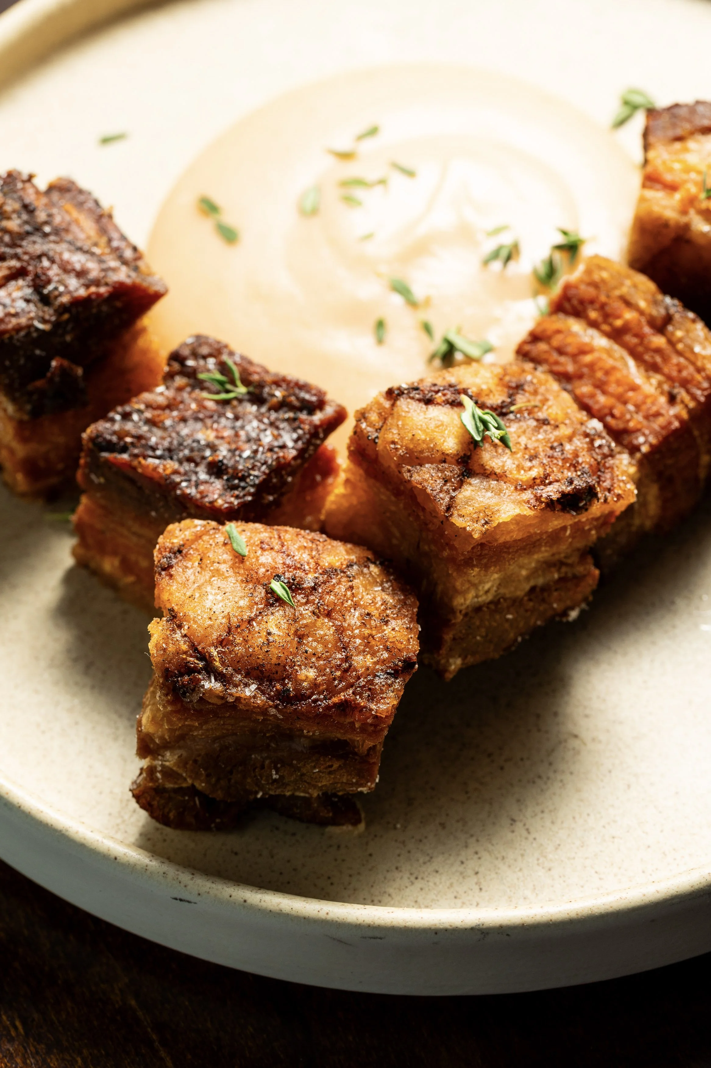 Fried pork belly cubes with a creamy dipping sauce on a beige plate.