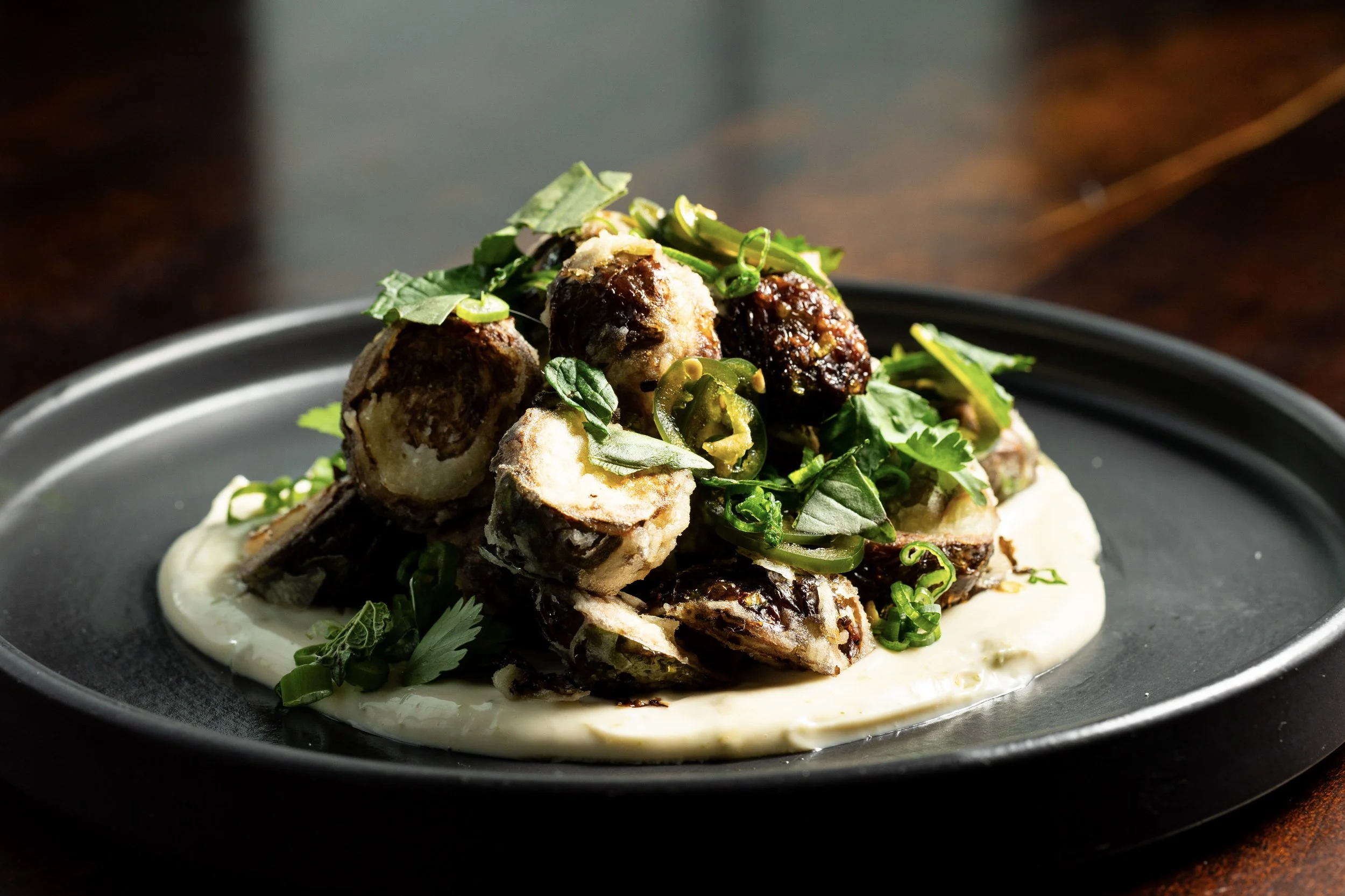 Plate of cooked mushrooms garnished with green herbs and sliced green chili peppers, served on a bed of white sauce or cream.