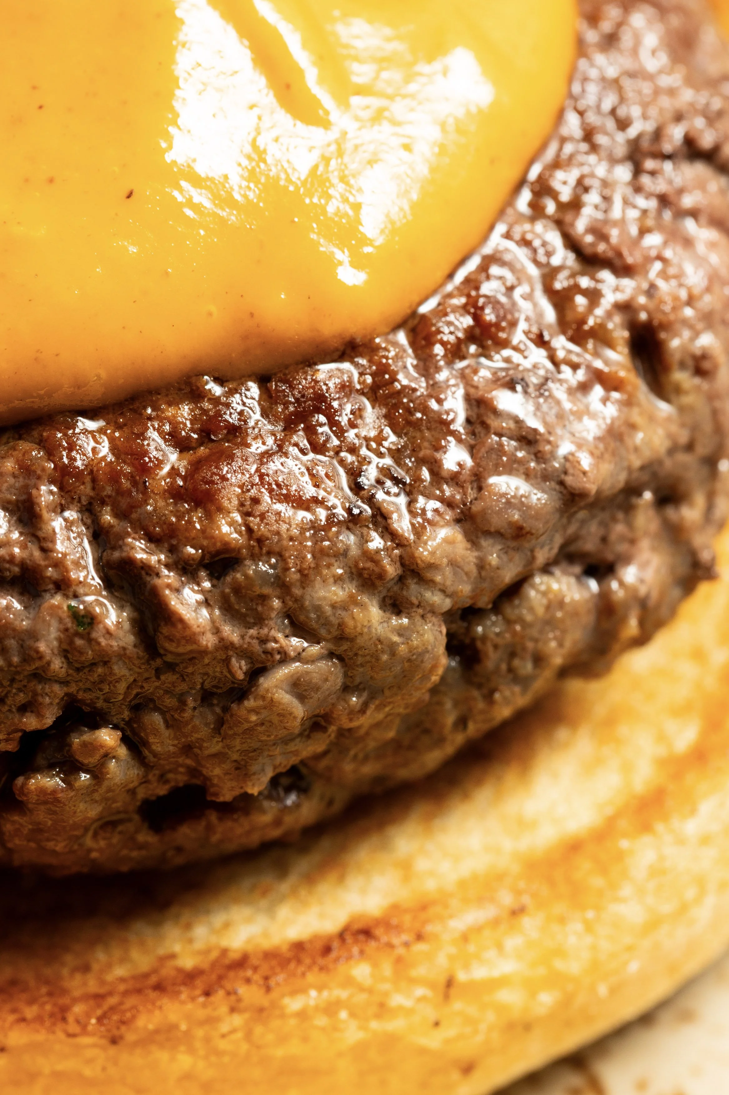 Close-up of a cooked hamburger patty topped with a slice of melted cheese, on a toasted bun.