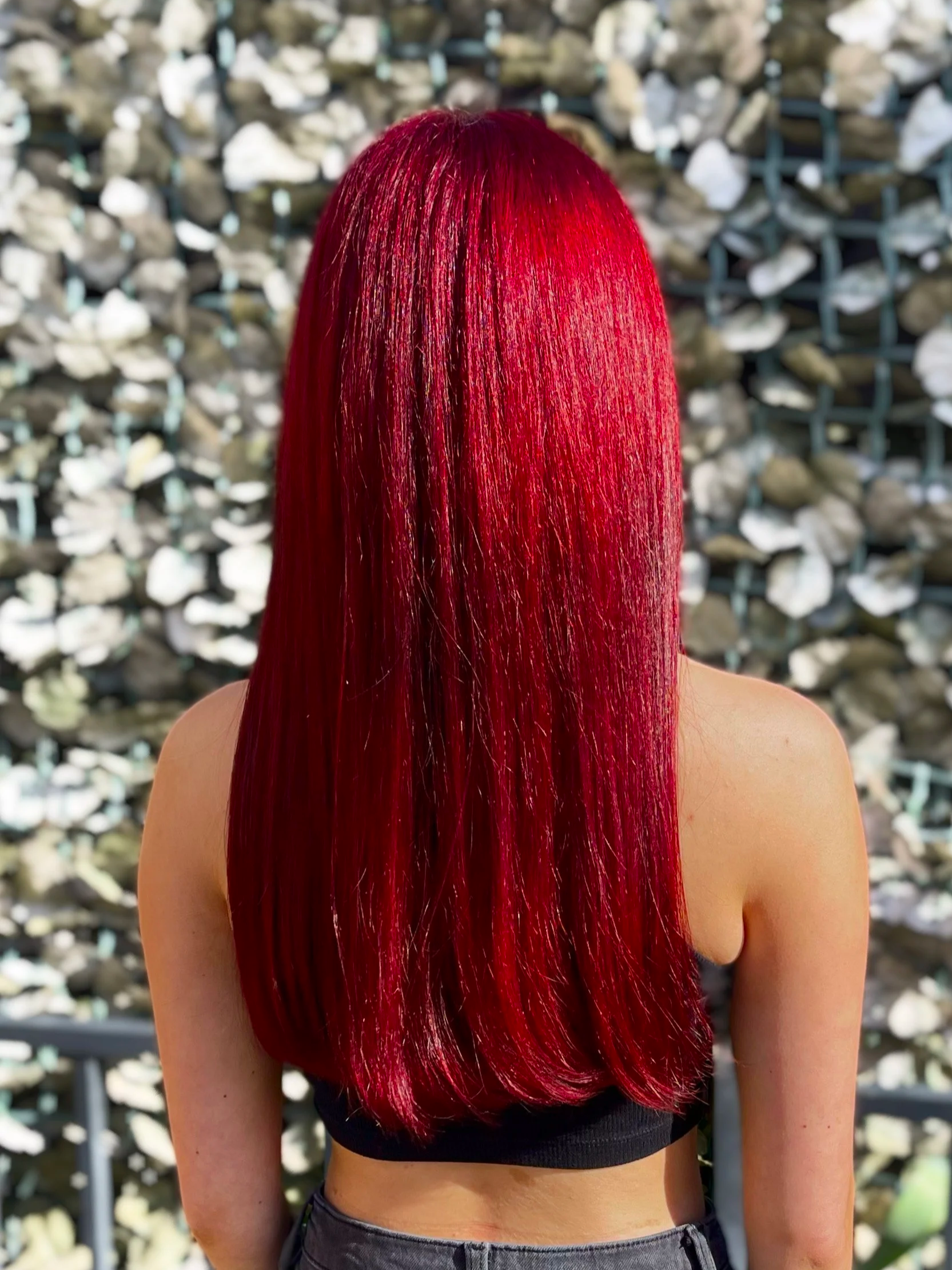 Back view of woman with long, straight, vibrant red hair outdoors against a rocky background.