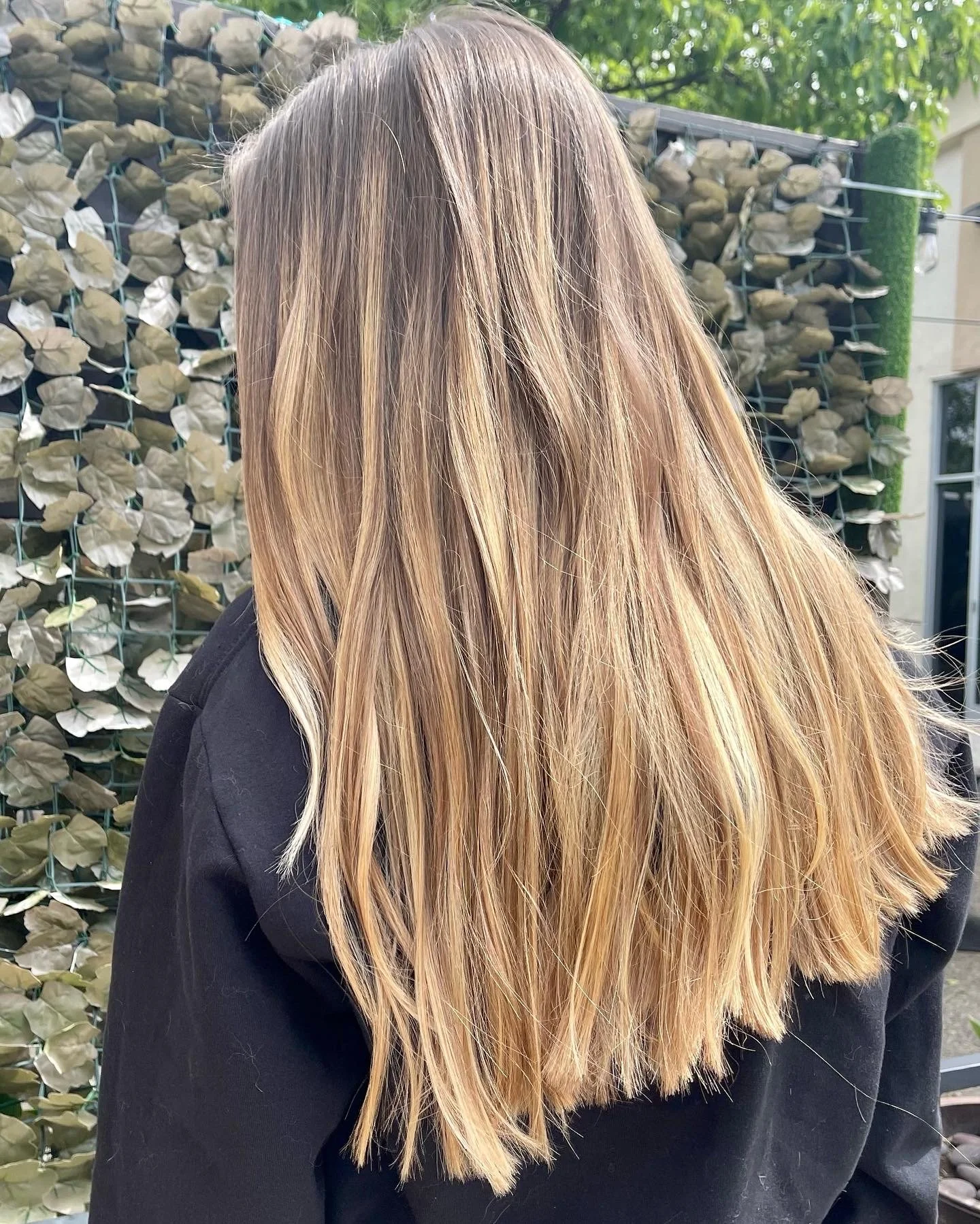 Back view of a woman with long, wavy blonde hair standing outdoors.