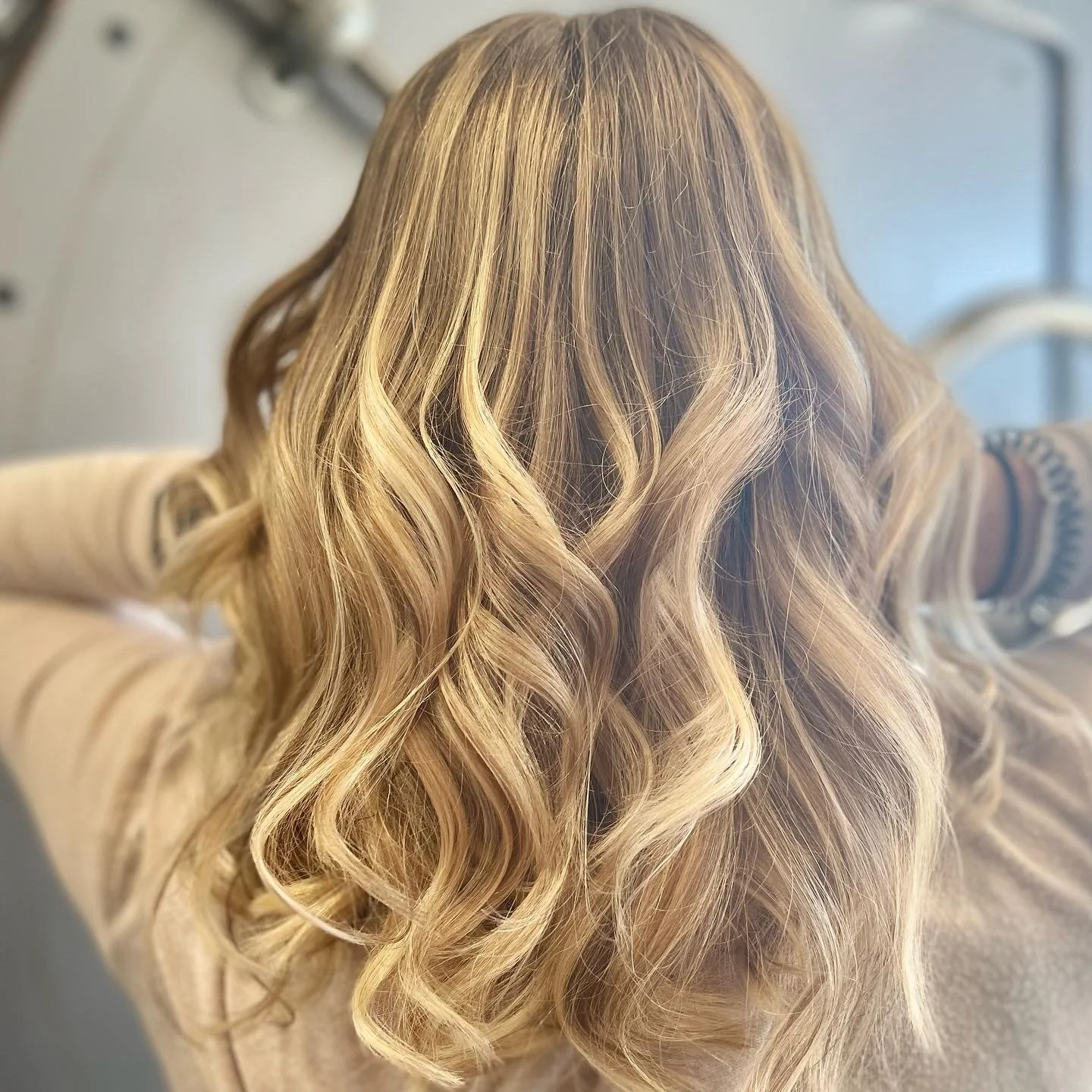 A person with long, blonde, wavy hair sitting with their back to the camera.