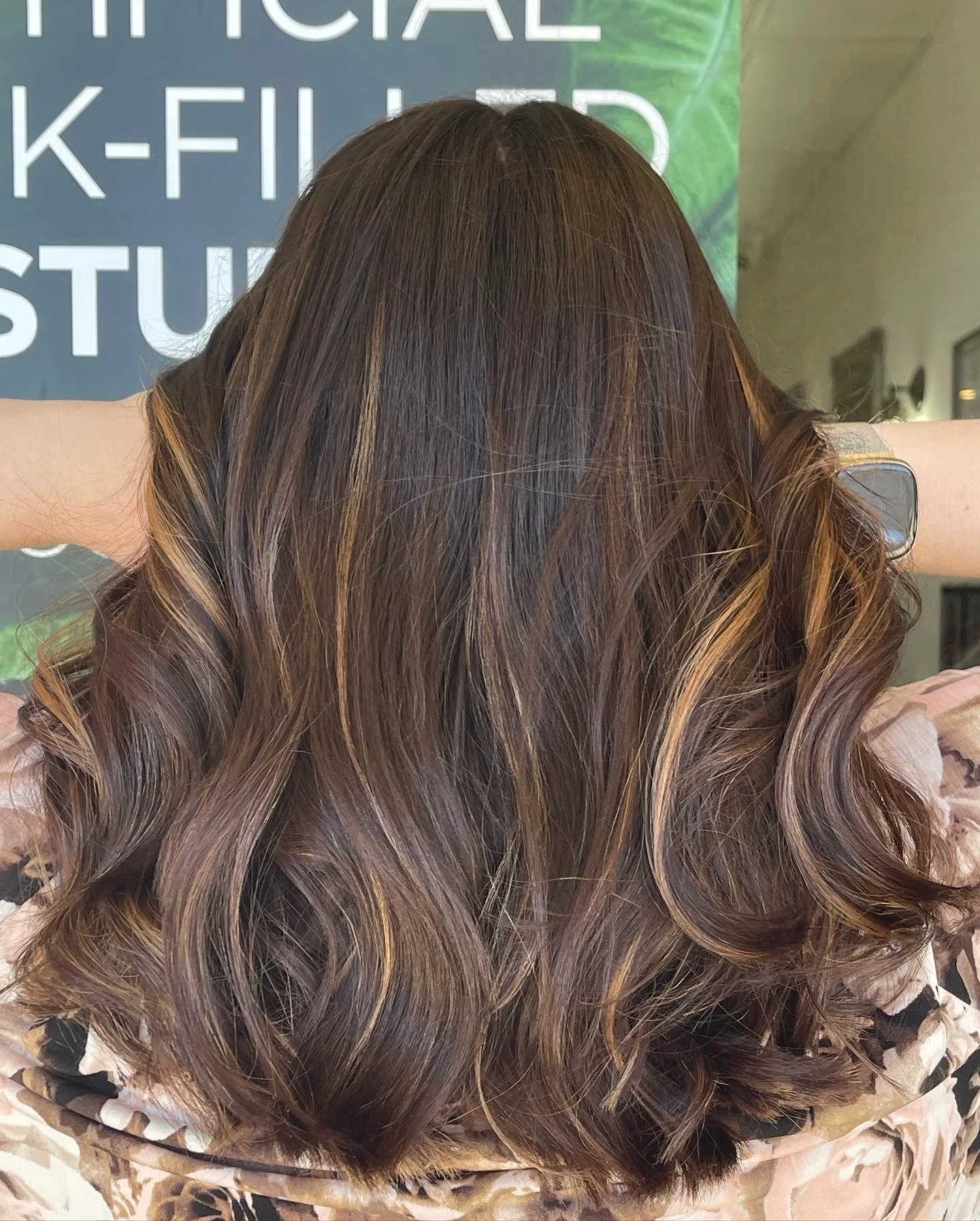 Back view of a person with long, wavy, brown hair with blonde highlights.