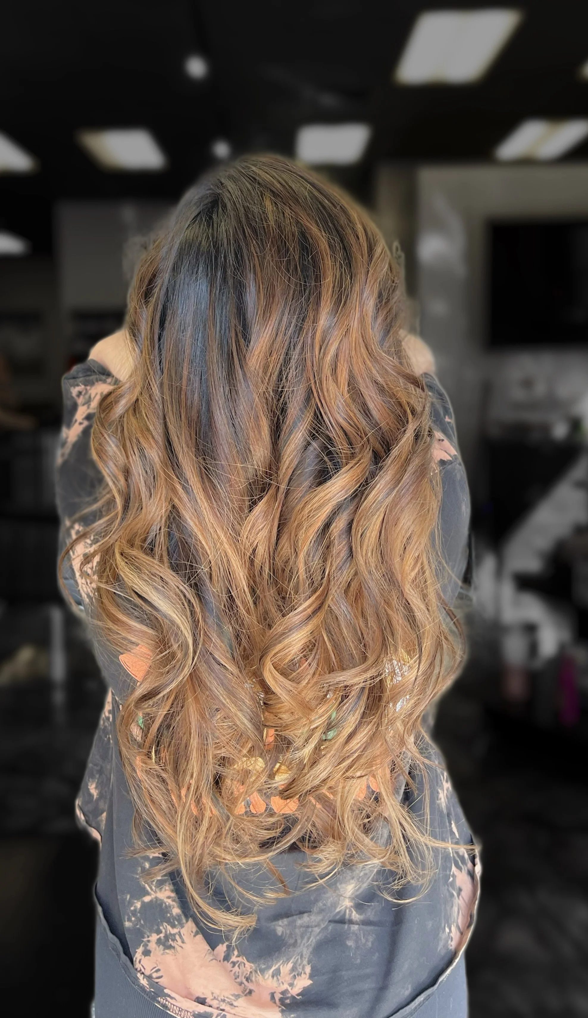 Back view of a woman with long, wavy, ombre hair transitioning from dark brown to blonde.