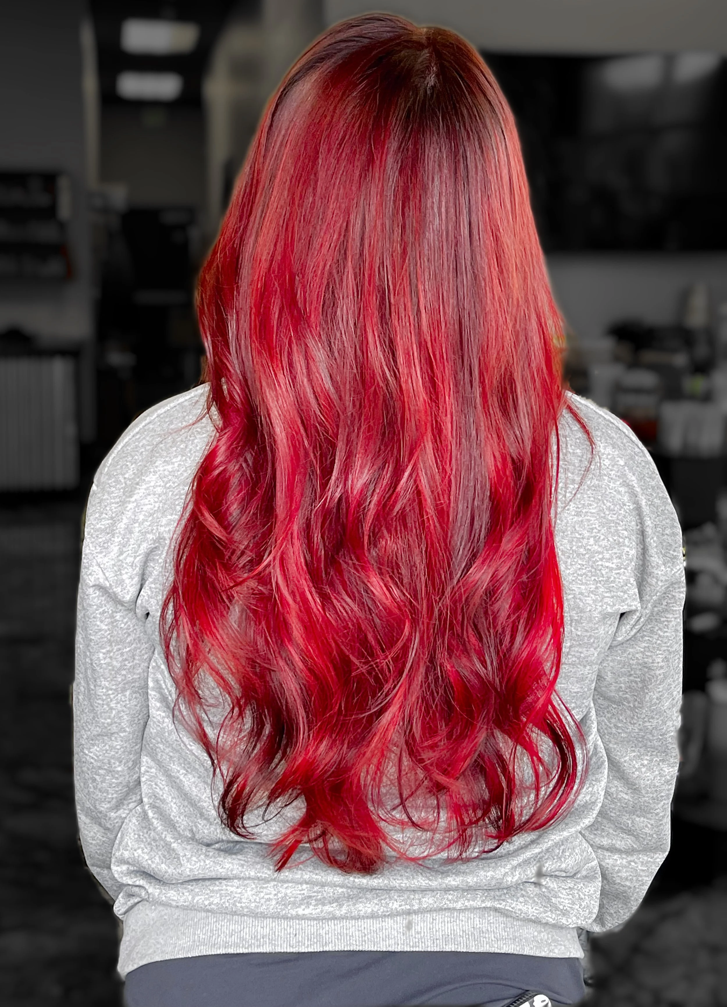 Back view of a person with long, wavy, vibrant red hair, wearing a light gray sweatshirt.