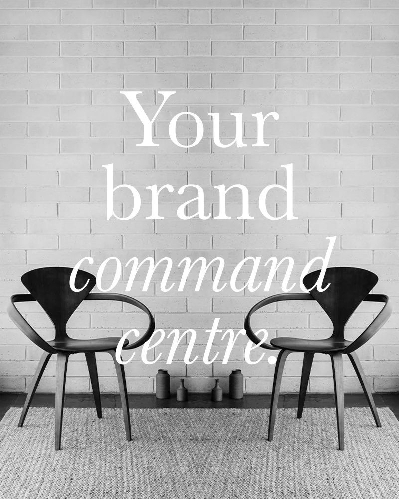 A black and white image of two modern chairs with curved backrests facing each other against a white brick wall. Four small vases are on the floor between the chairs, and a textured rug covers the floor. Overlaid text reads 'Your brand command centre.'