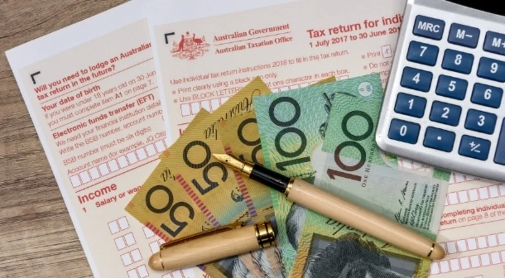 Australian tax documents with Australian currency notes, a pen, and a calculator on a wooden surface.