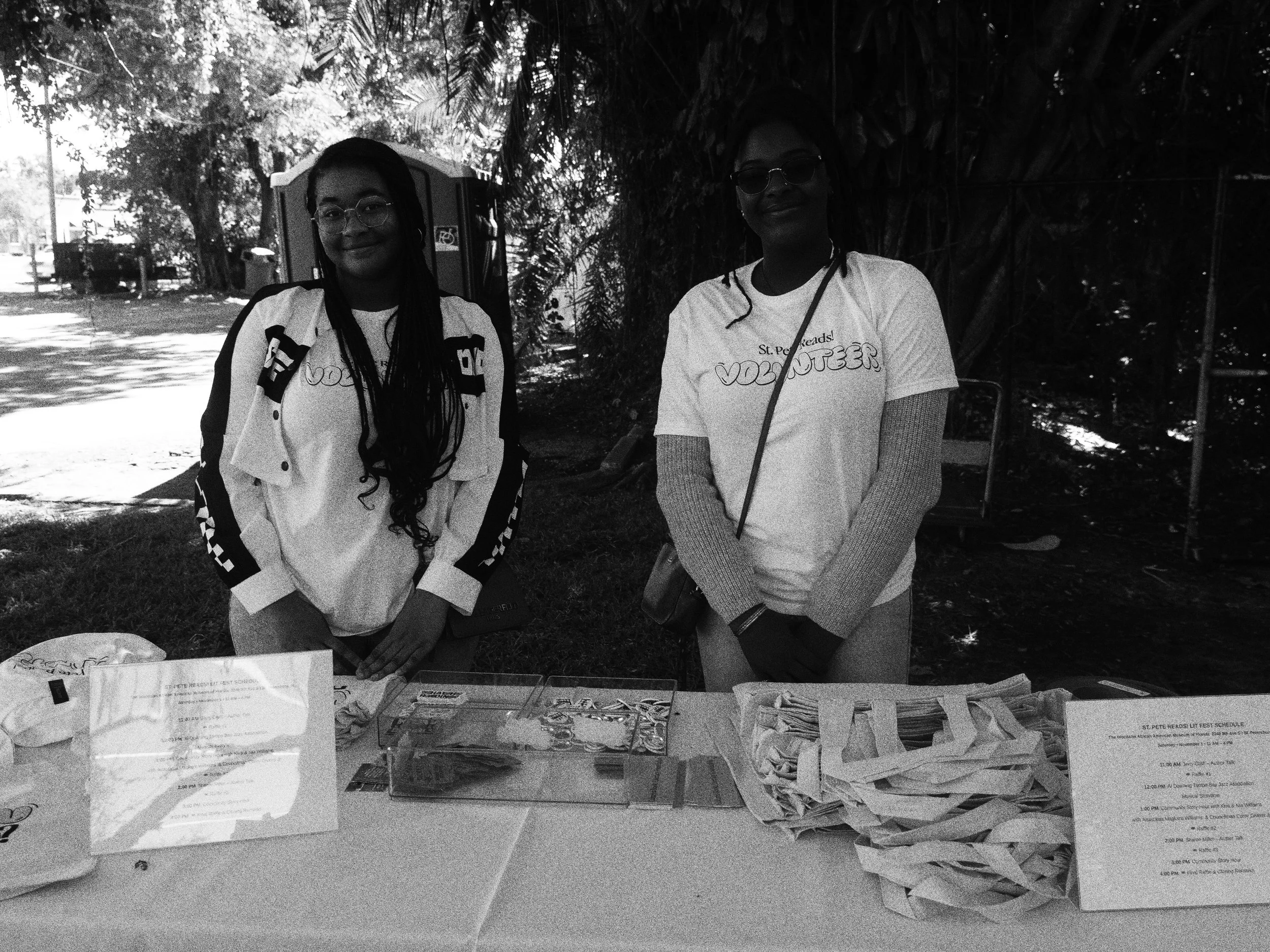 Two St. Pete Reads! Lit Fest volunteers welcome families at an outdoor festival table in St. Petersburg, Florida.