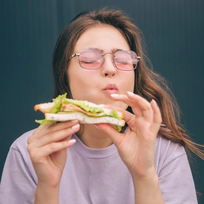 Woman with glasses eating a sandwich with lettuce, turkey, and bread.