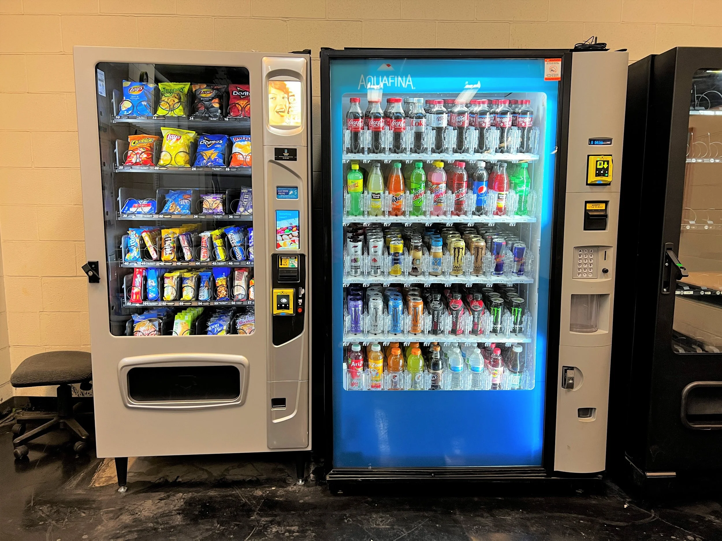 Two vending machines side by side; the left one offers snacks including chips, and the right one dispenses bottled soft drinks.